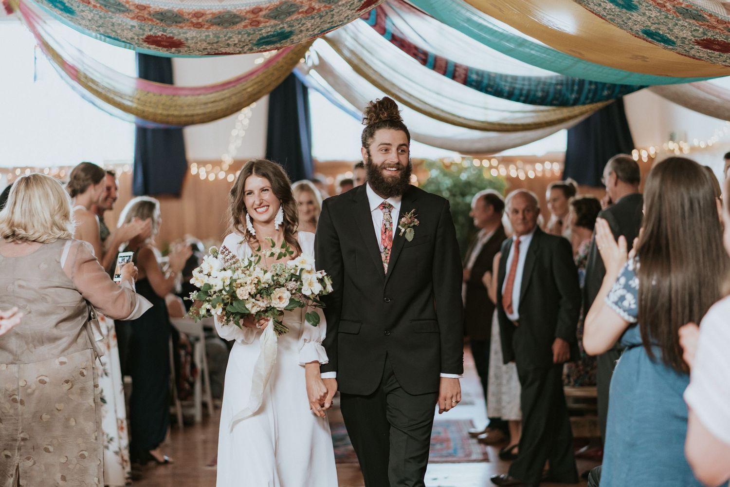 Wedding guests celebrating outdoors under elegant drapes and string lights during an evening reception.