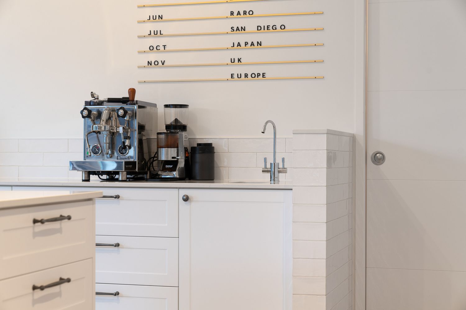 Clean white kitchen counter with professional coffee machine setup and minimalist menu board.
