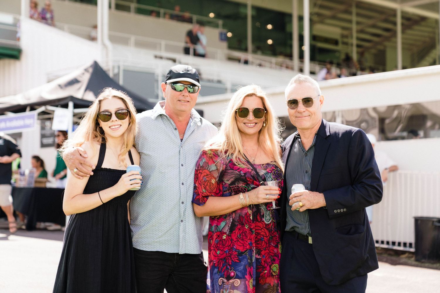 Four people in stylish outfits gather at an outdoor venue during a sunny day event.