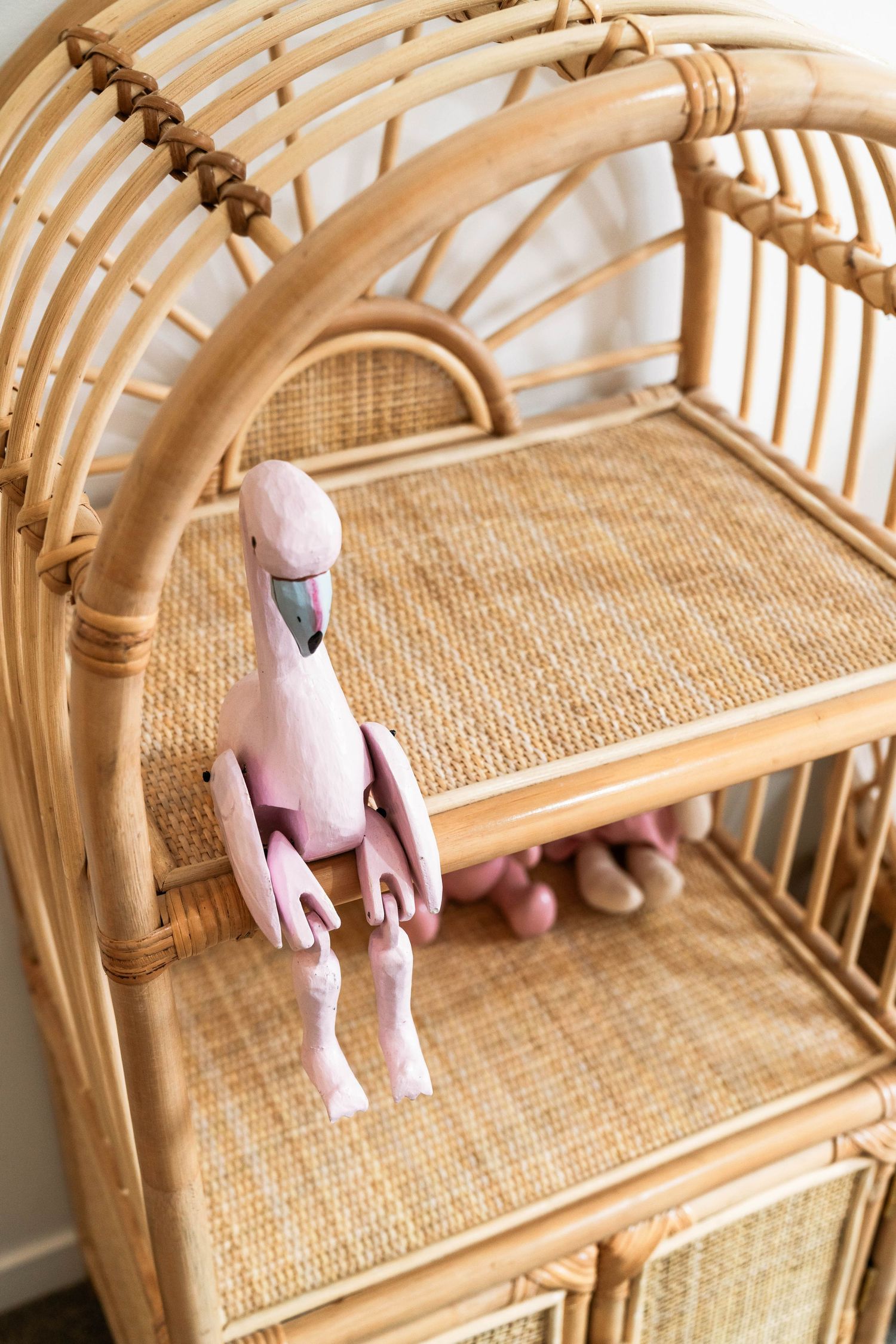 Pink stuffed bunny toy sitting on a natural rattan bamboo shelf unit with woven details.