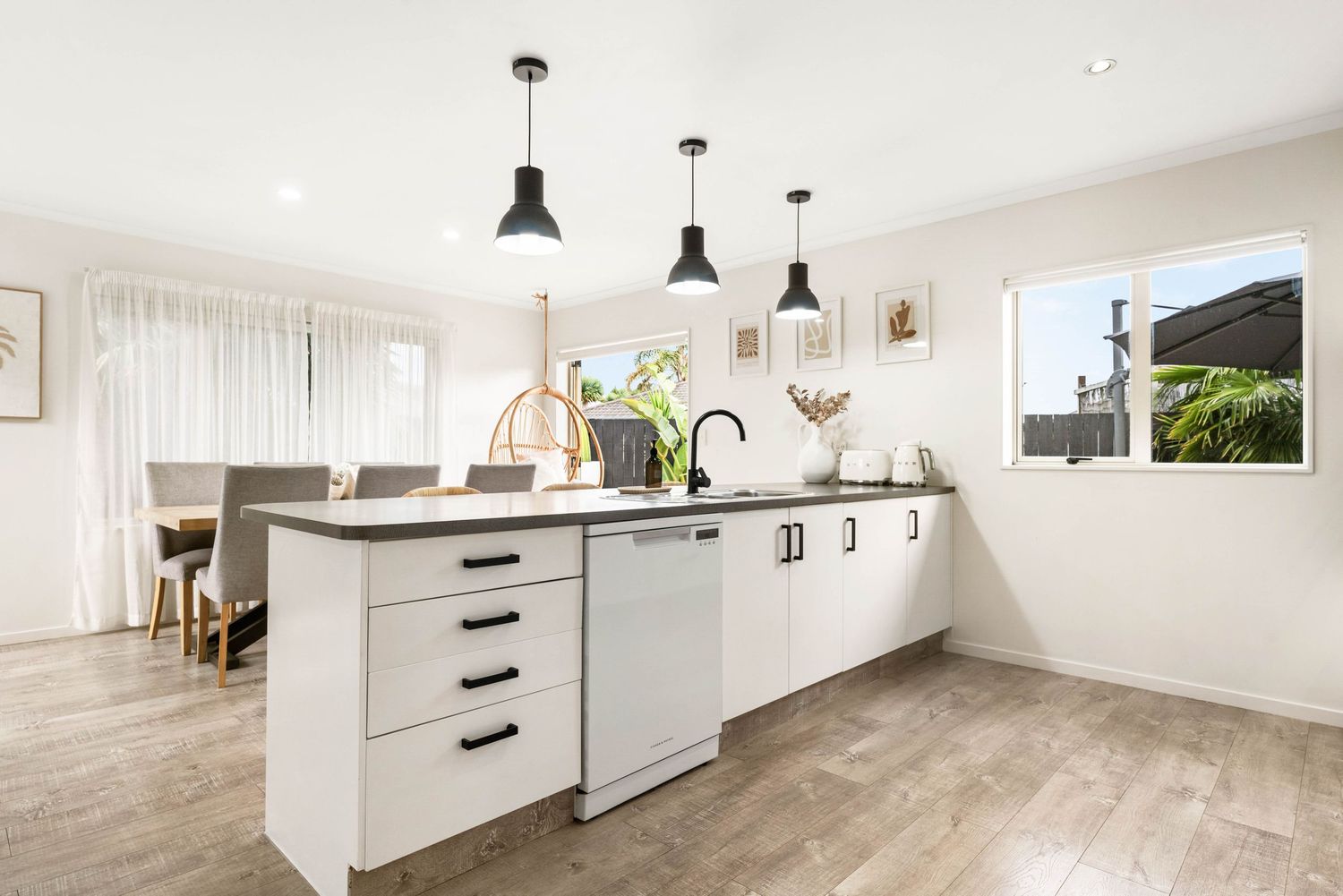Modern white kitchen interior with hardwood flooring, pendant lights, and custom cabinetry showcases minimalist design style.