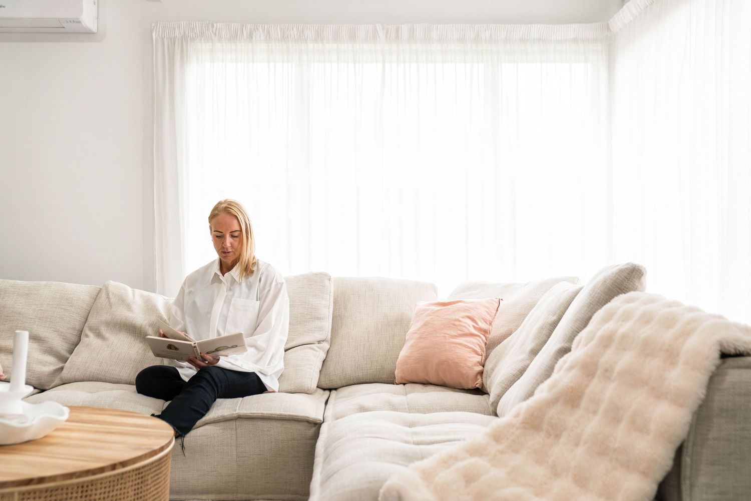 Person relaxing on a light colored sectional sofa with throw pillows in a bright modern living room.