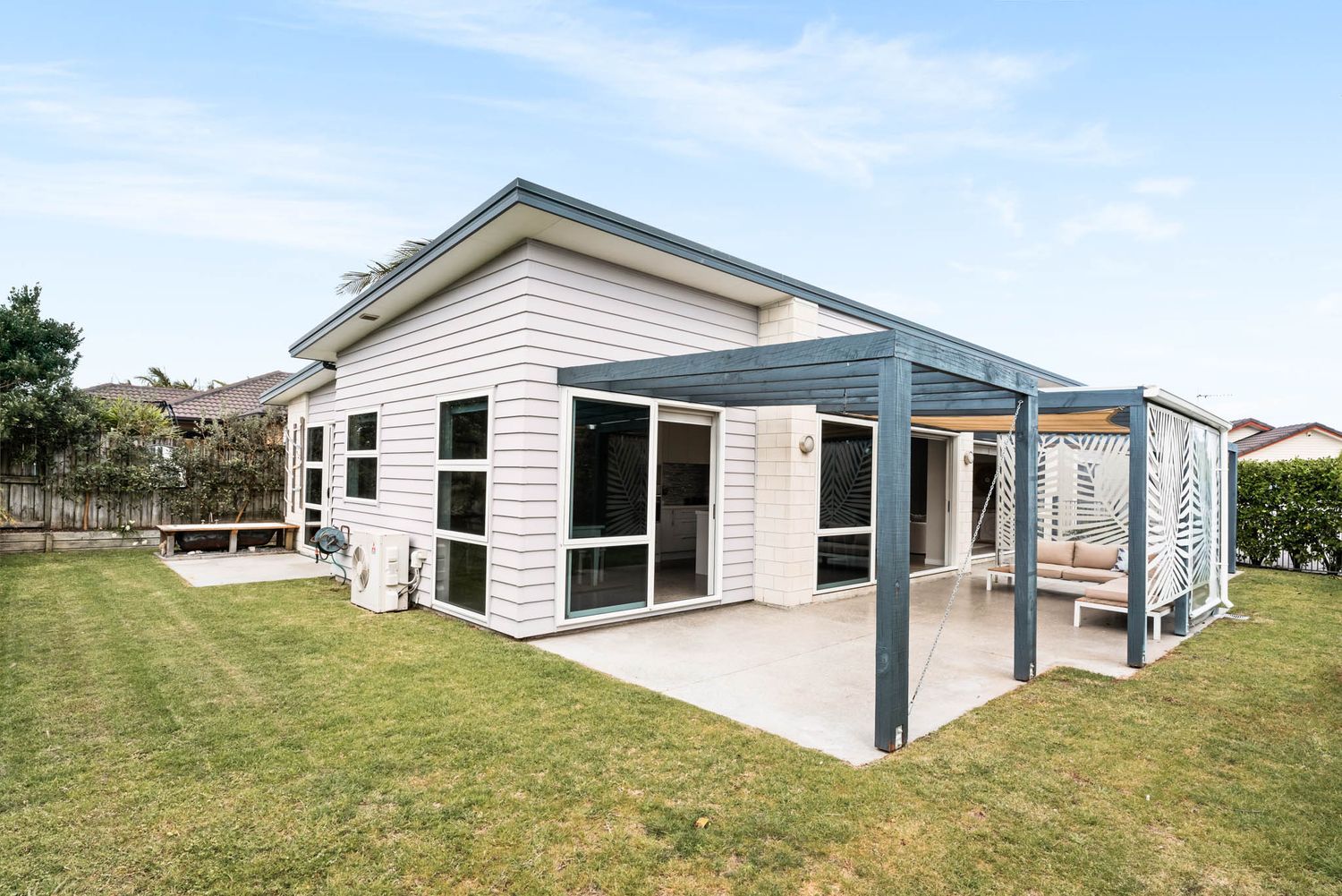 Modern white single-story house with covered patio and manicured lawn features large windows and contemporary design.