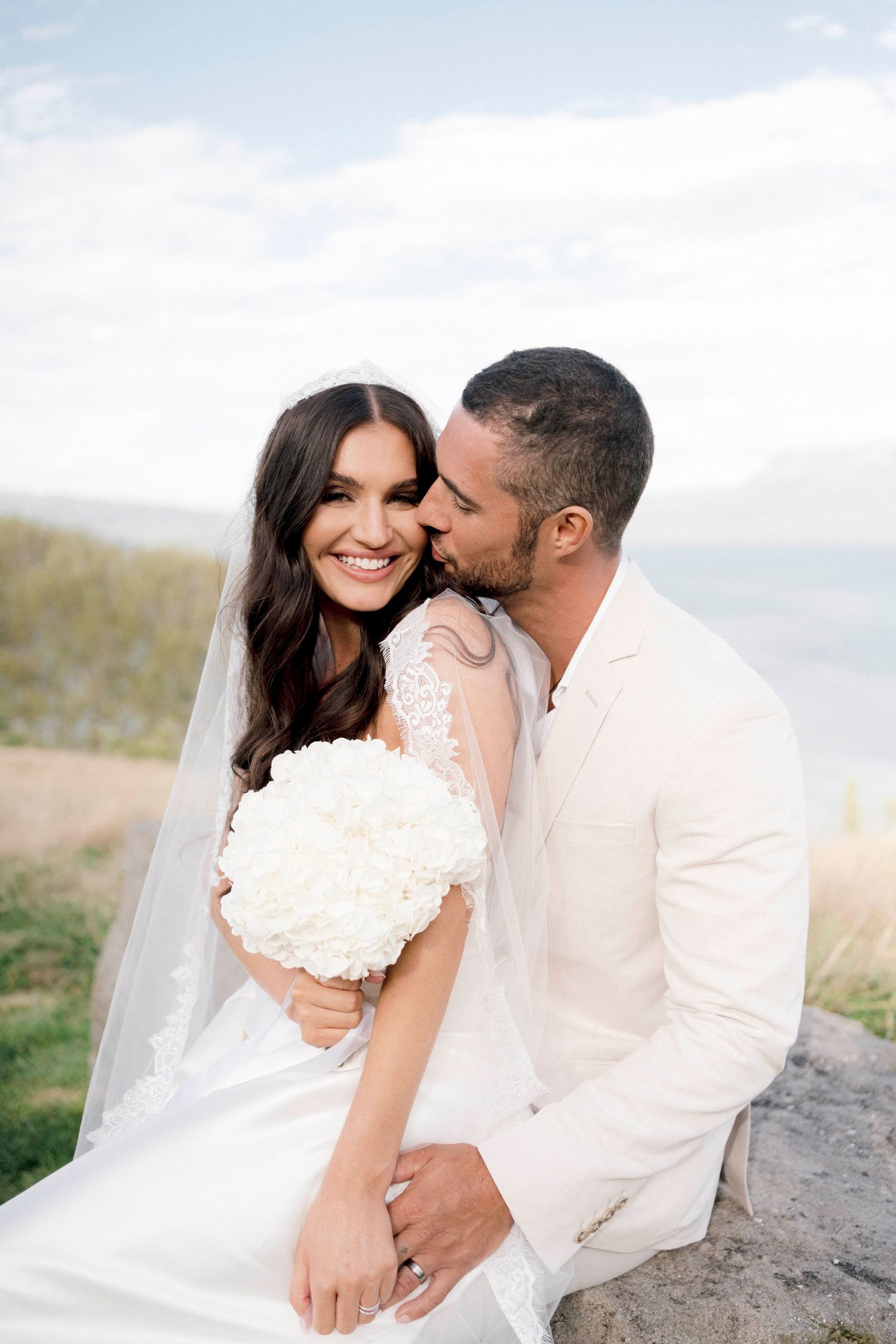 A tender wedding moment captured in golden light with white attire and floral bouquet.