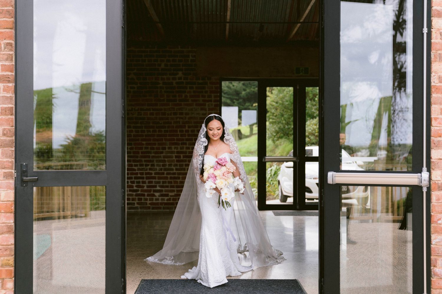 Wedding party entrance at a rustic brick venue with modern white columns and glass doors.