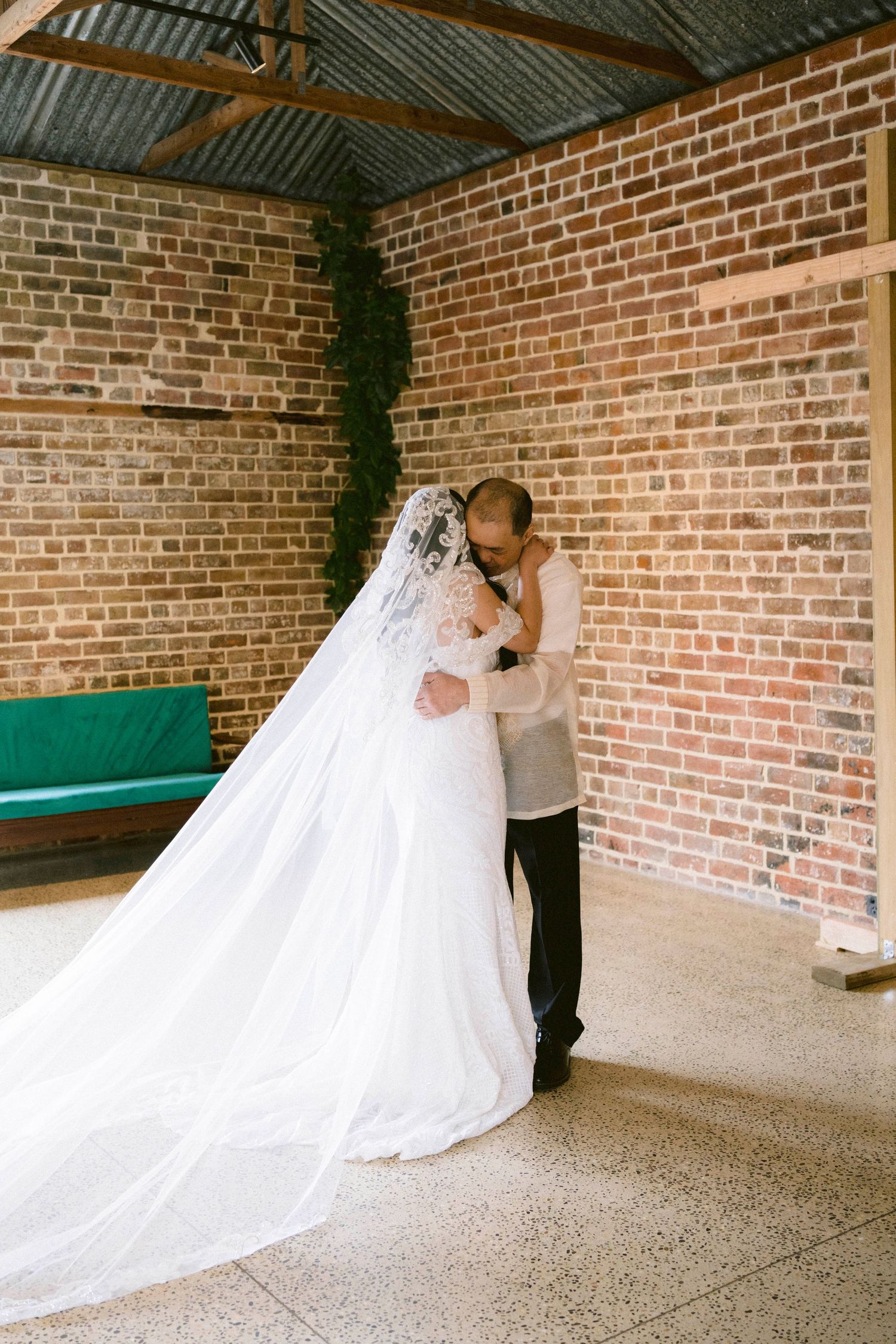 Intimate wedding moment in a rustic brick-walled room with long flowing veil.