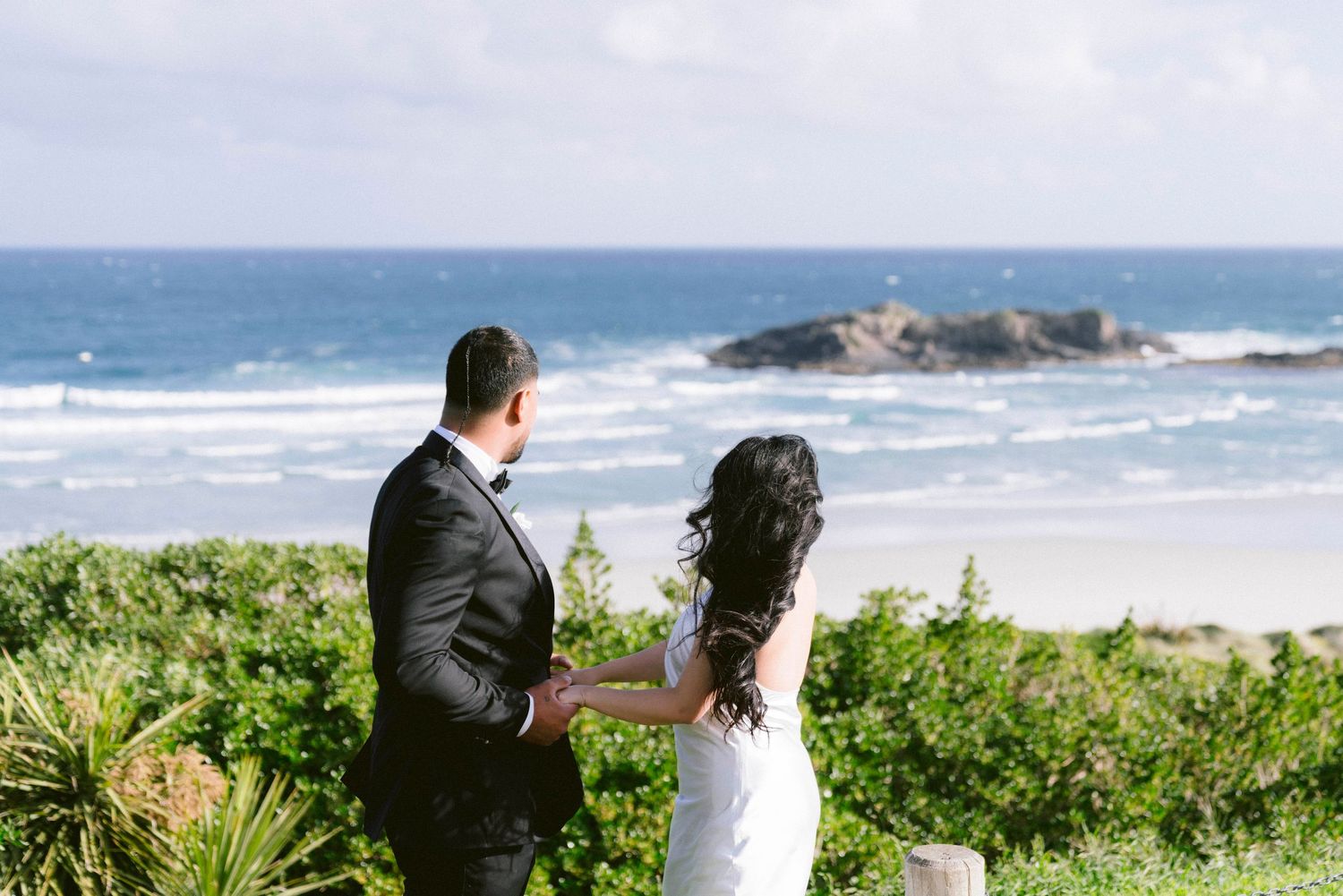 Newlyweds share an intimate moment overlooking a scenic ocean coastline.