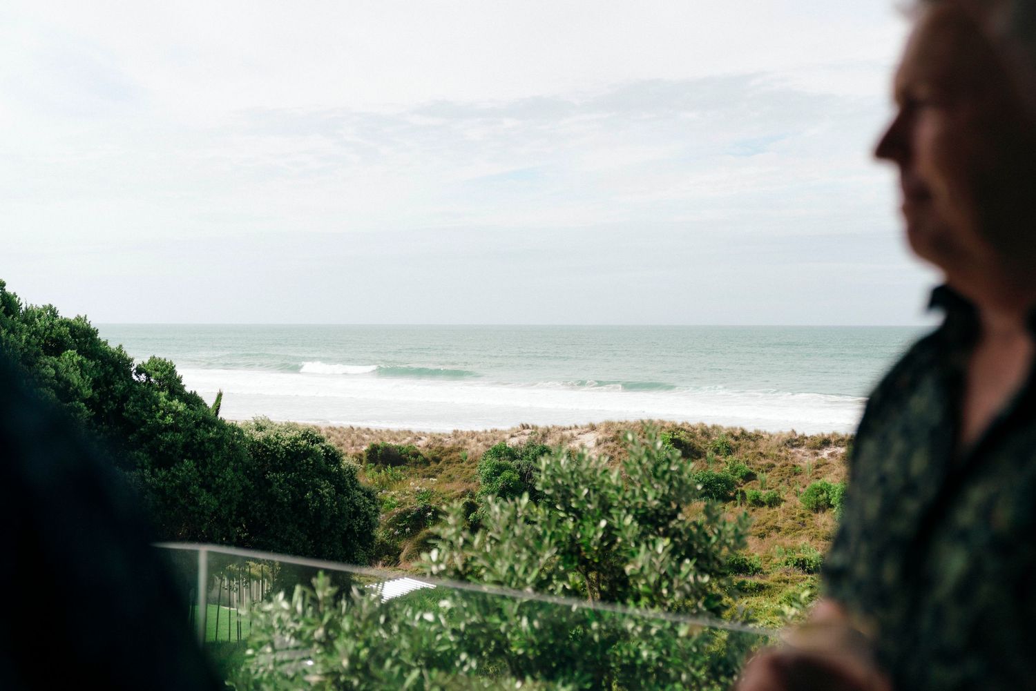 Panoramic coastal view of ocean waves crashing against a sandy beach under cloudy skies.