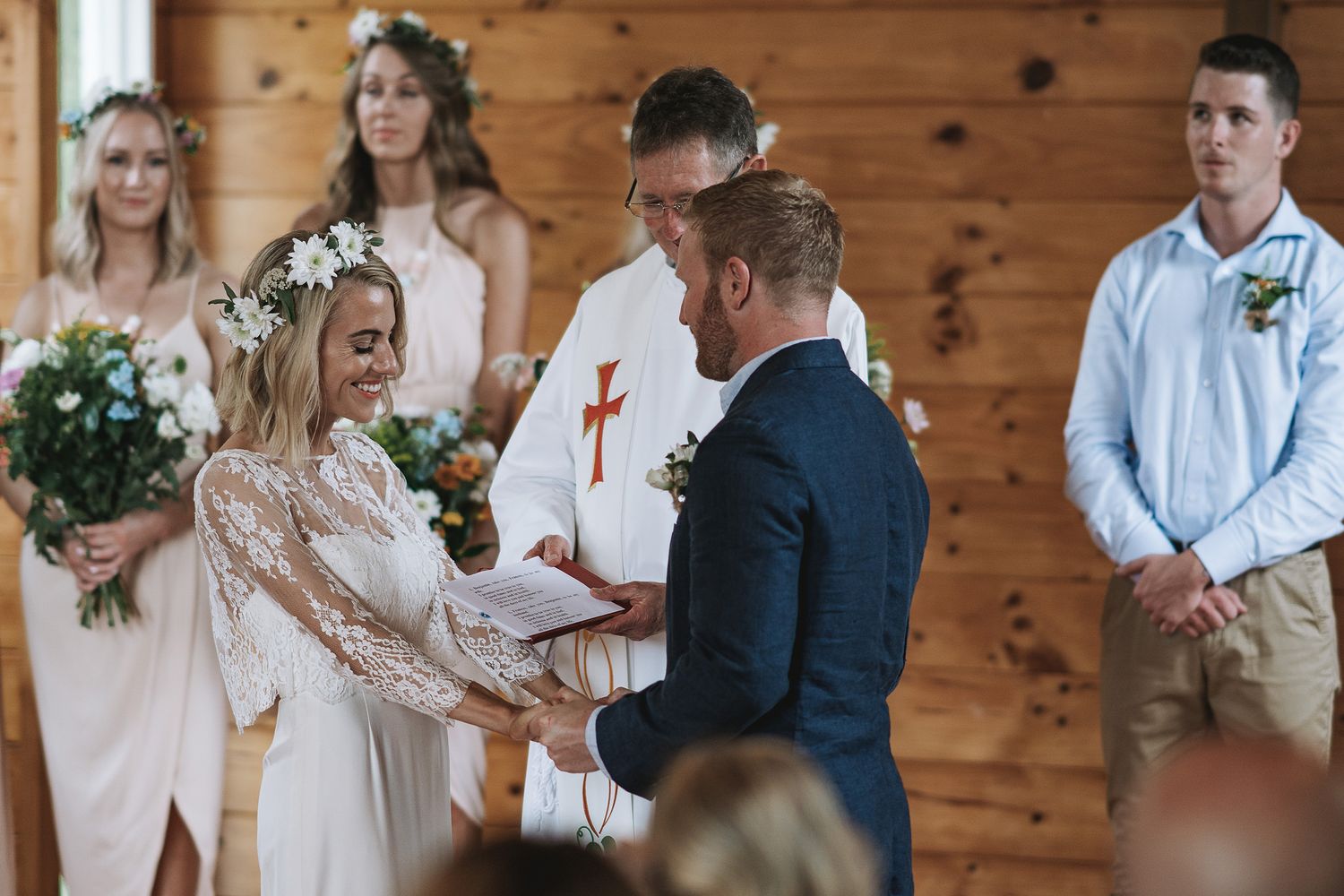A couple exchanges vows during a rustic indoor wedding ceremony with bridesmaids and groomsmen looking on.