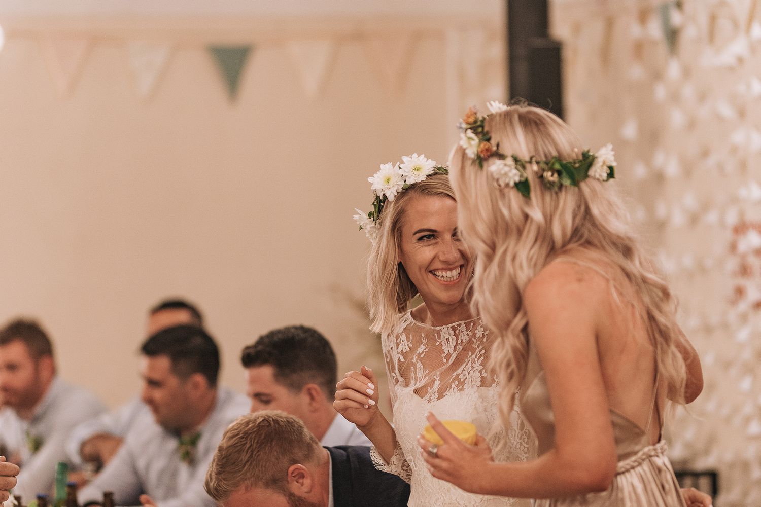 Two people share a joyful moment at a wedding reception with white decor and string lights in the background.