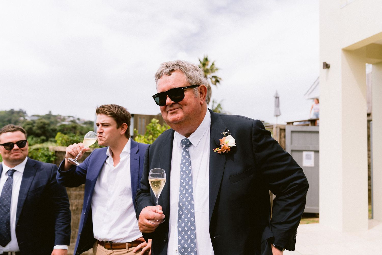 Wedding guests mingling outdoors on a sunny day wearing formal attire.