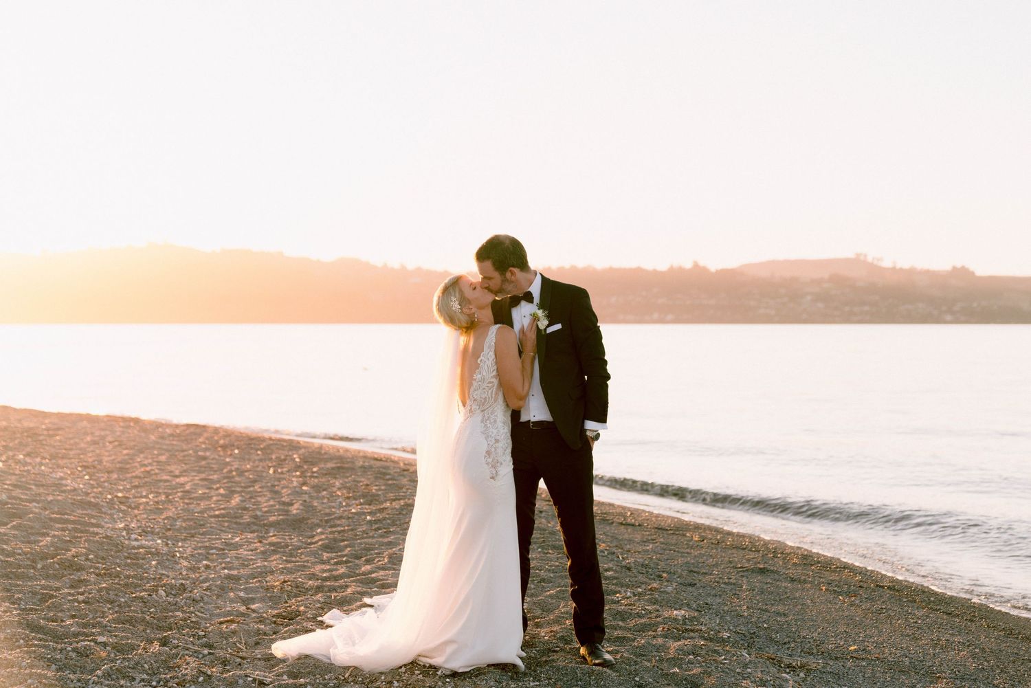 Couple embraces on scenic beach at sunset with warm golden light reflecting off the water.