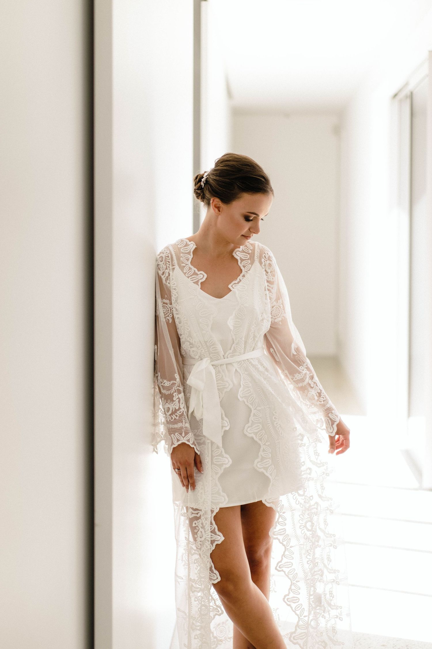 Ethereal bridal boudoir photo featuring delicate lace robe in bright white hallway.