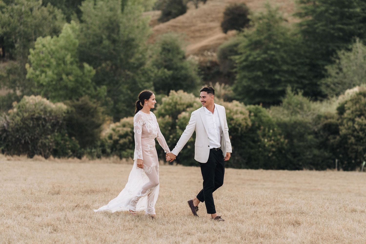 Couples walk hand in hand across a sunlit meadow during a wedding celebration.