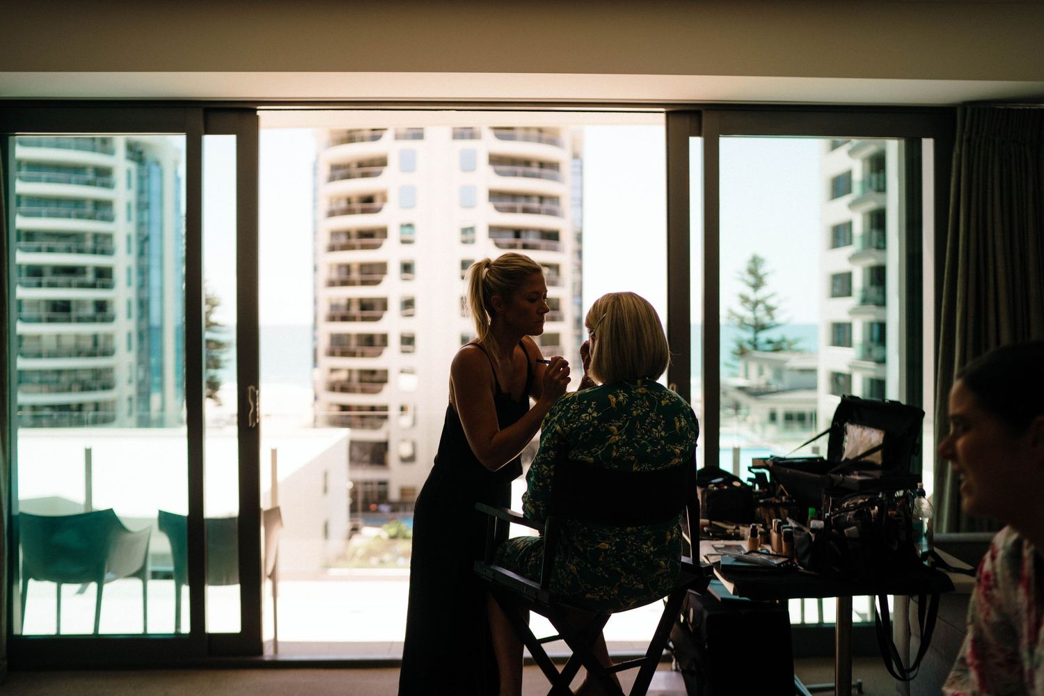 Silhouetted figures by large windows overlooking urban high-rise buildings during golden hour at home.