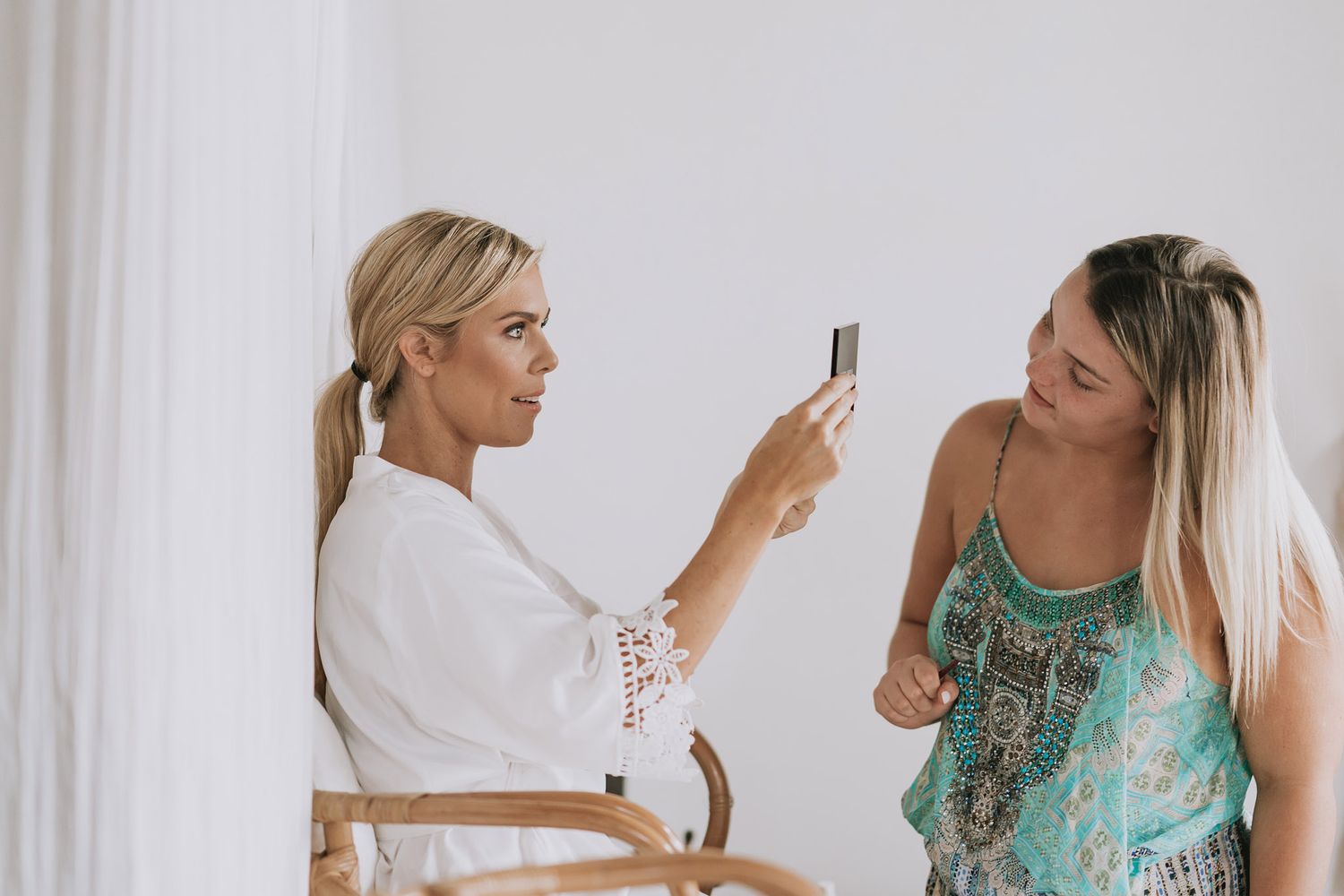 A sequence of images showing a blonde woman in a teal dress laughing and taking selfies in front of a white curtain.