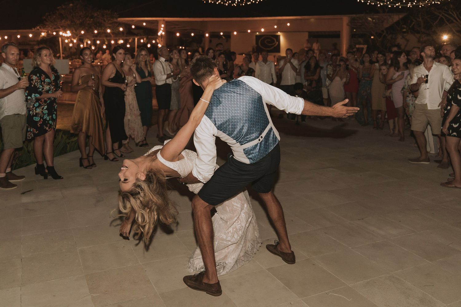 Wedding guests dancing and celebrating on an outdoor dance floor under string lights.