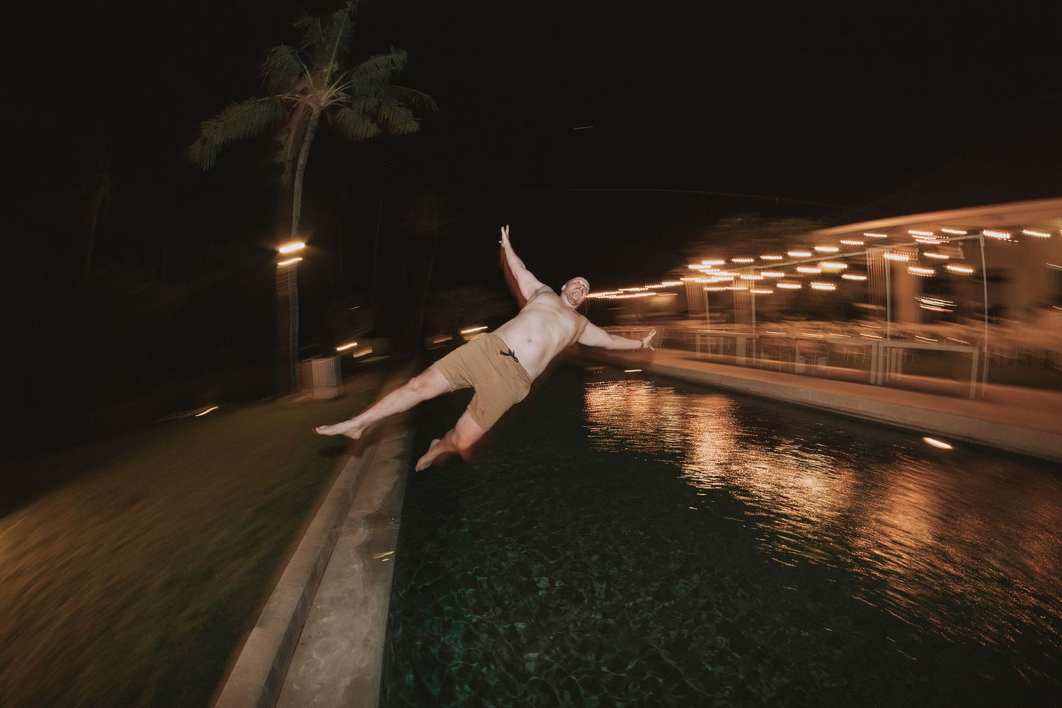 Nighttime poolside wedding reception with glowing lights reflecting on the water.