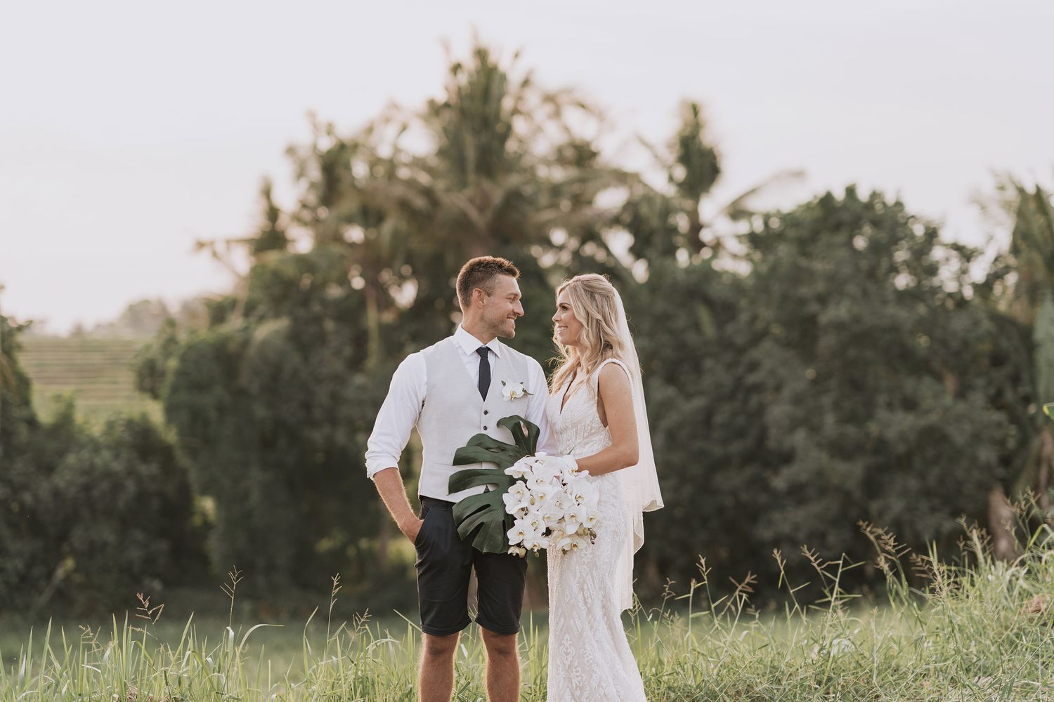 A couple shares an intimate moment on a grassy hillside during their rustic outdoor wedding ceremony.