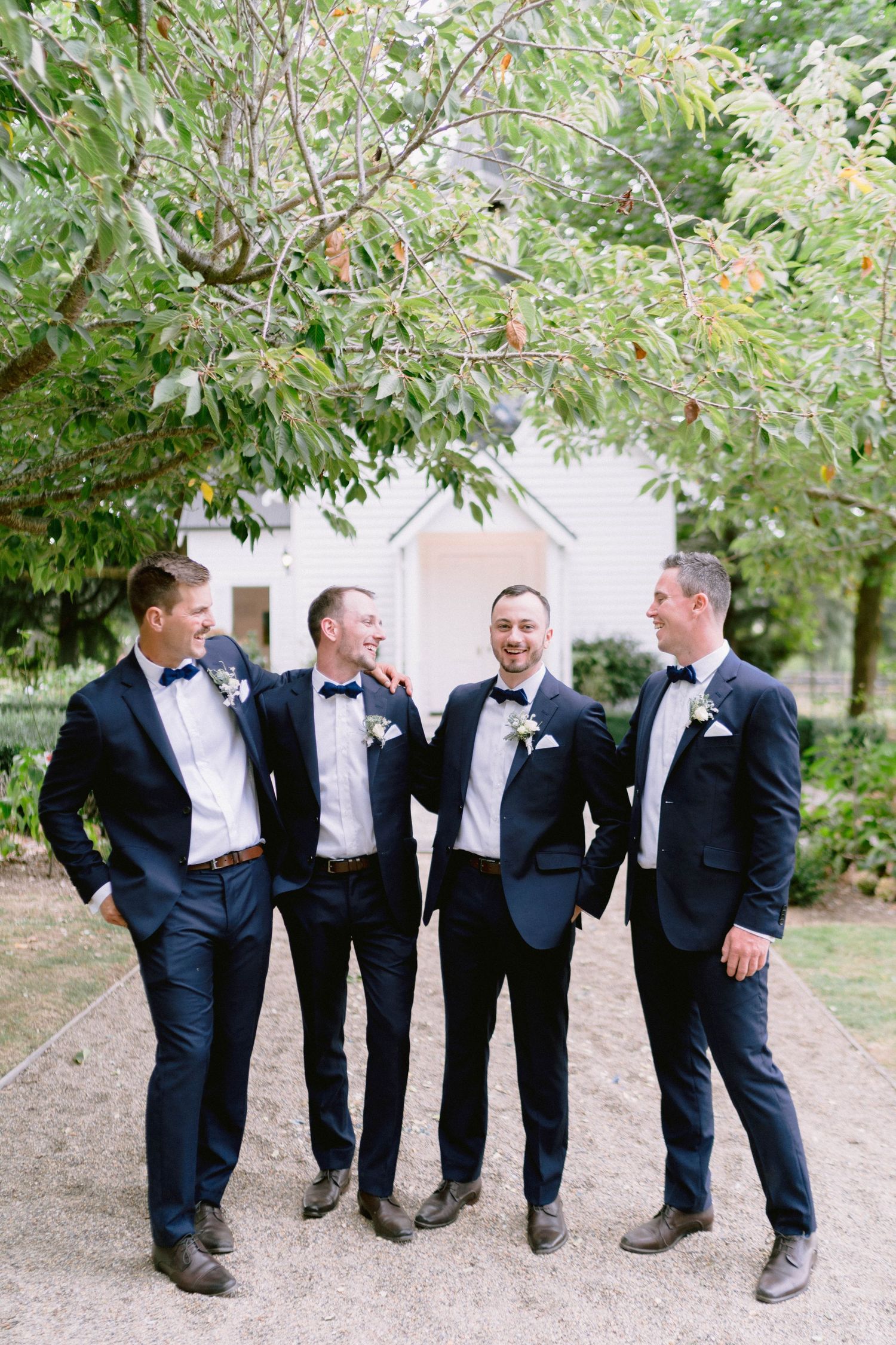 Groomsmen in black tuxedos sharing a lighthearted moment outdoors.