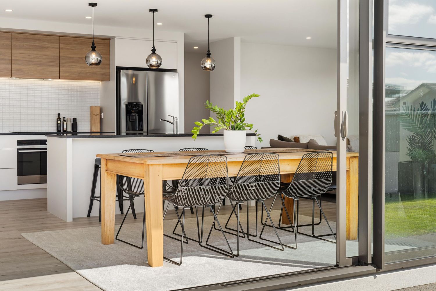 Modern kitchen and dining space with wooden table, wire chairs, pendant lights and sliding glass doors to garden.