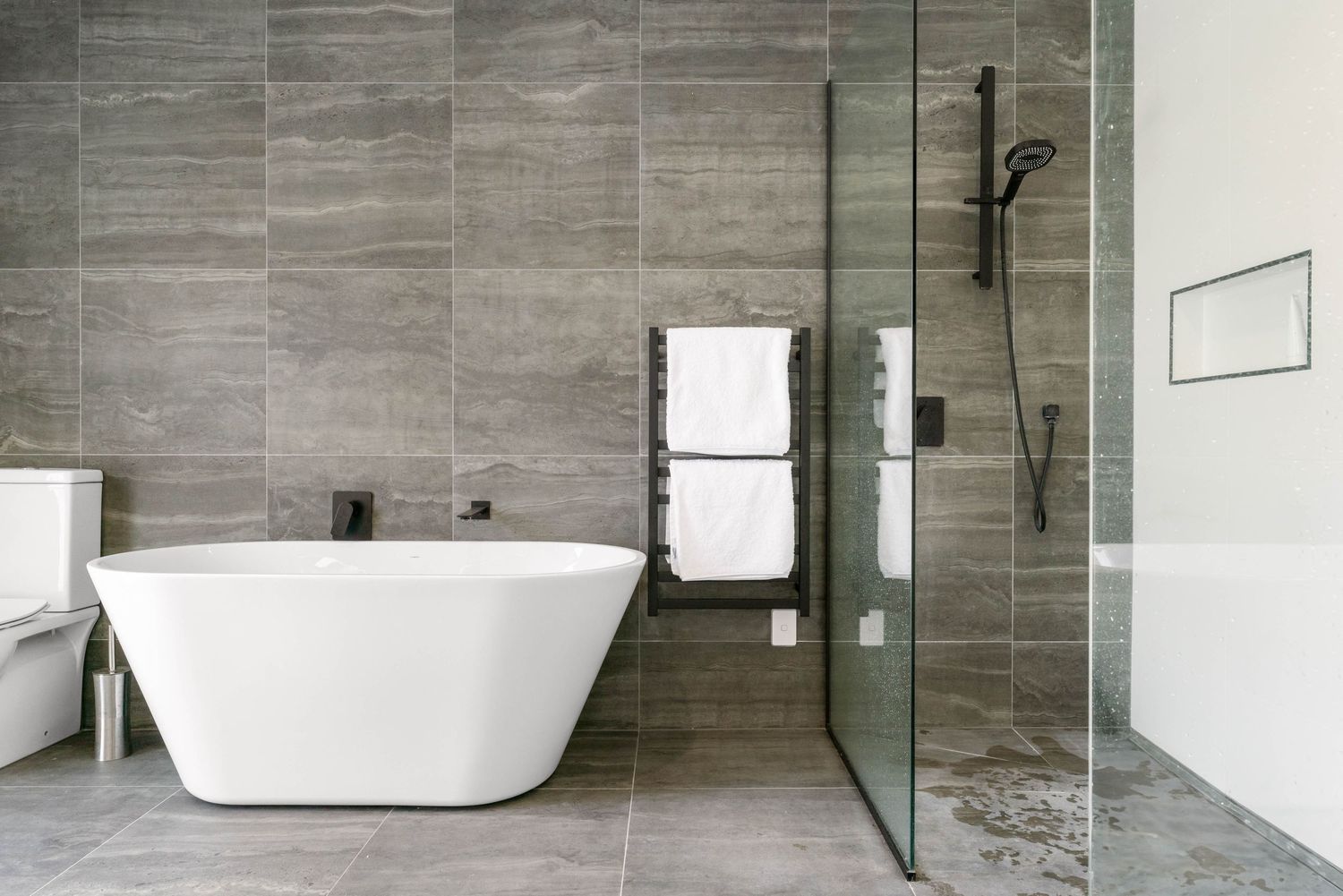 Luxury bathroom with grey tile walls, freestanding tub, and glass shower enclosure in modern minimalist design.
