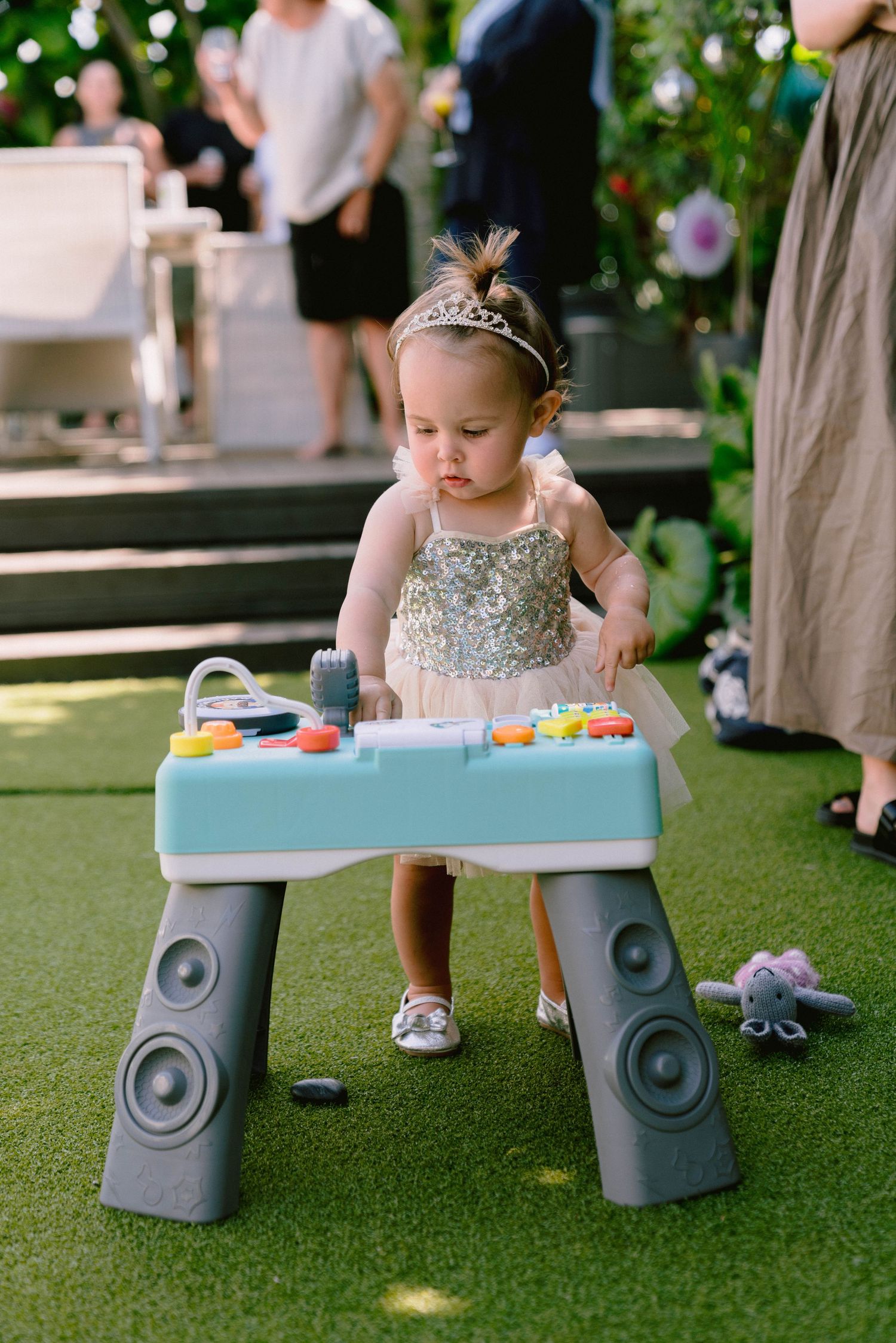 Child sits at a colorful activity table with built-in speakers on artificial grass during an outdoor event.