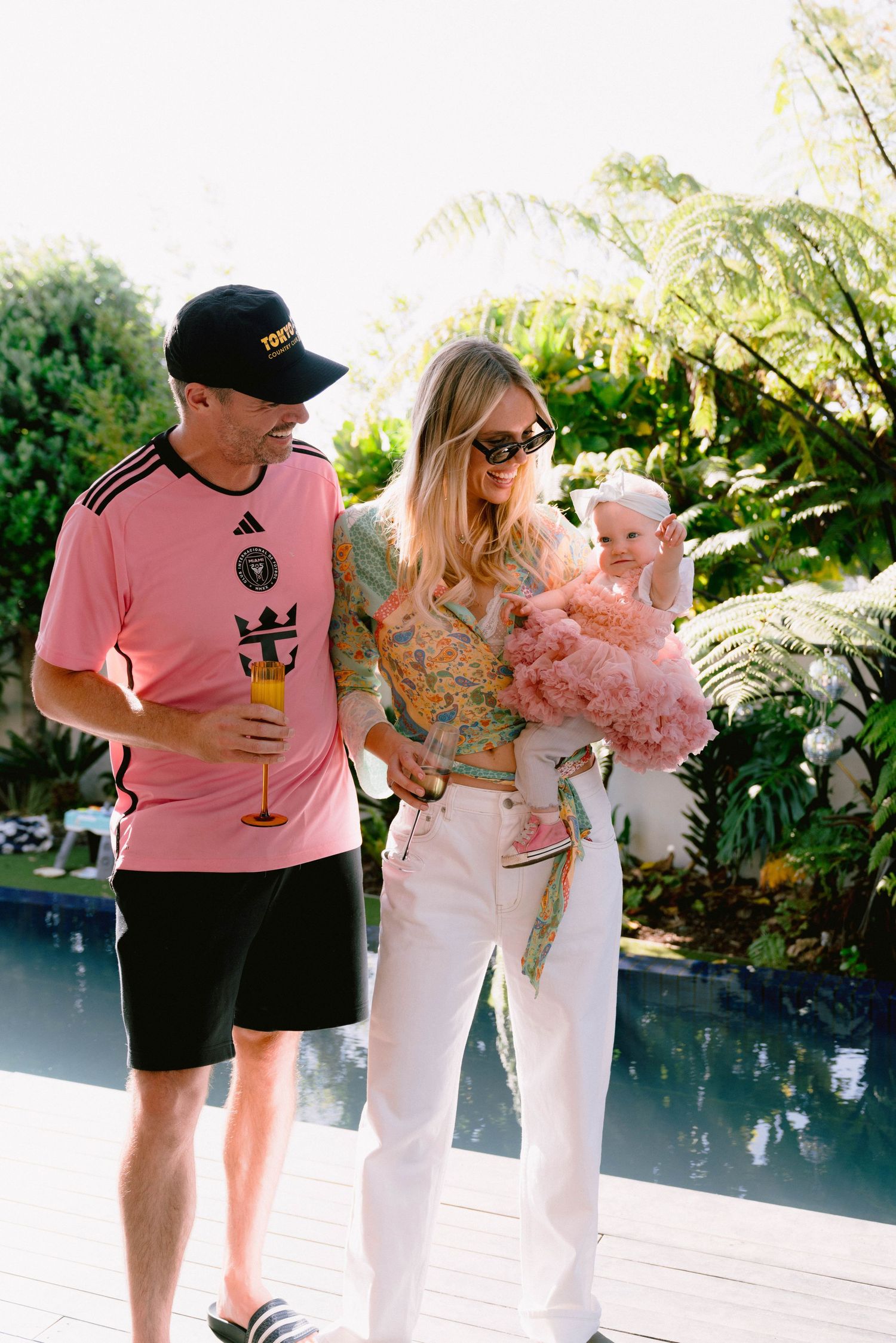 People socializing by a pool, with one holding a baby in pink dress.