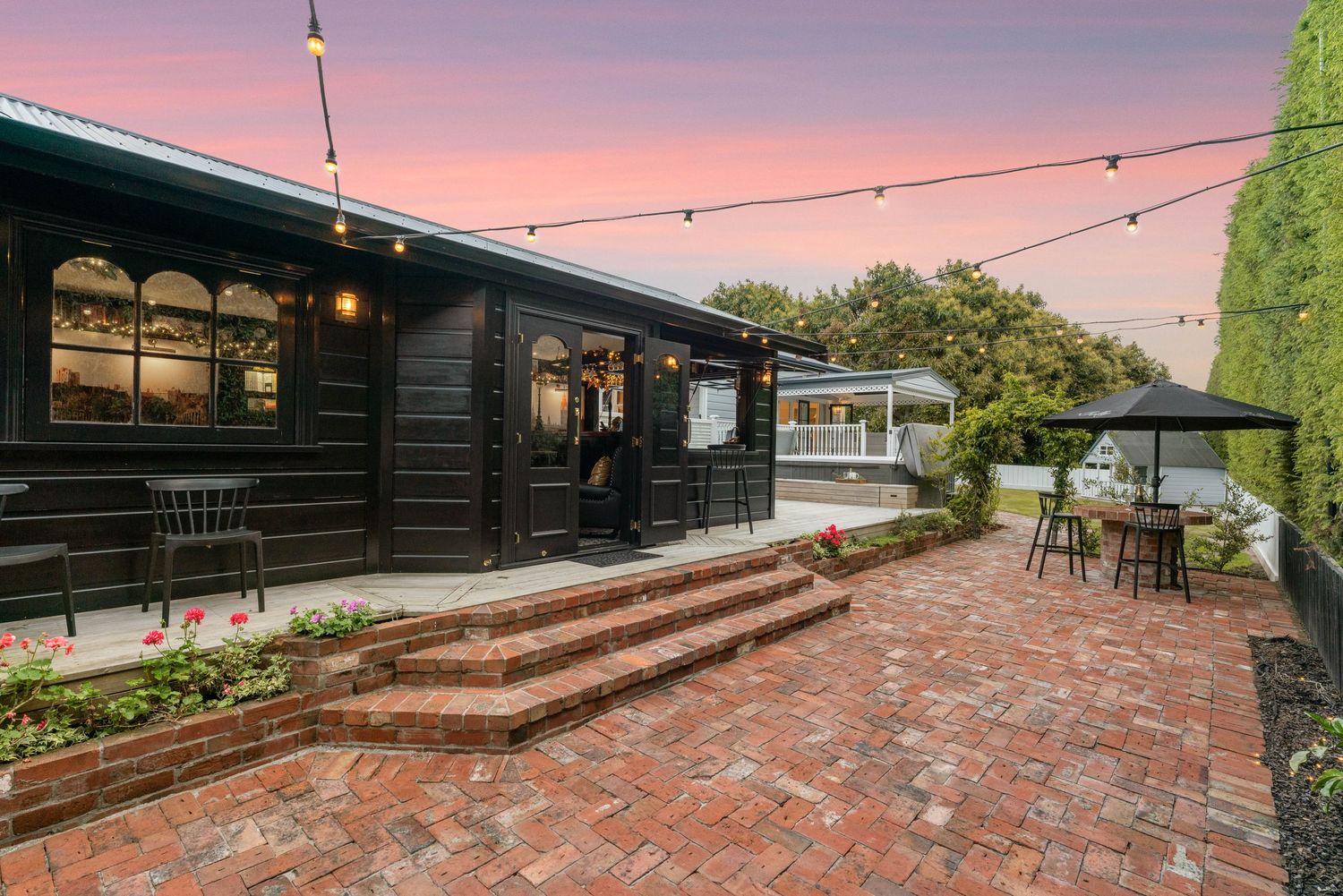 Contemporary backyard deck with string lighting and black exterior at dusk.