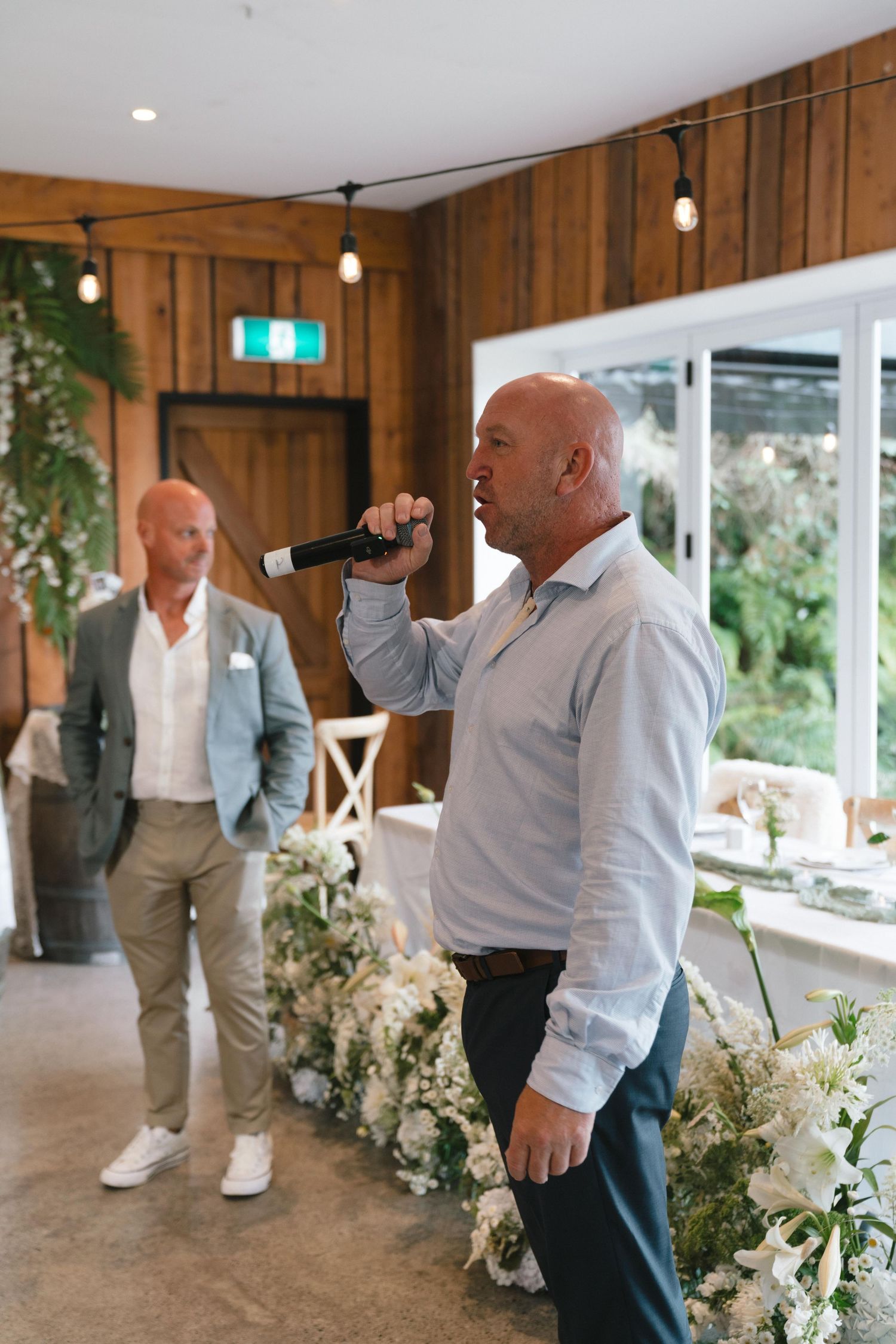 Wedding speaker delivers speech in rustic wooden venue with pendant lighting.
