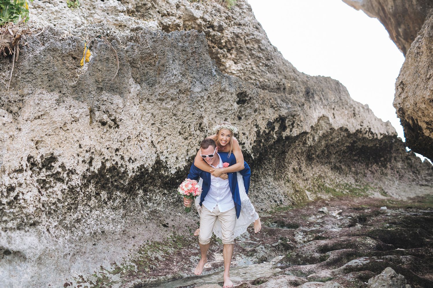 Couple posing playfully near rocky coastal formations on a beach.