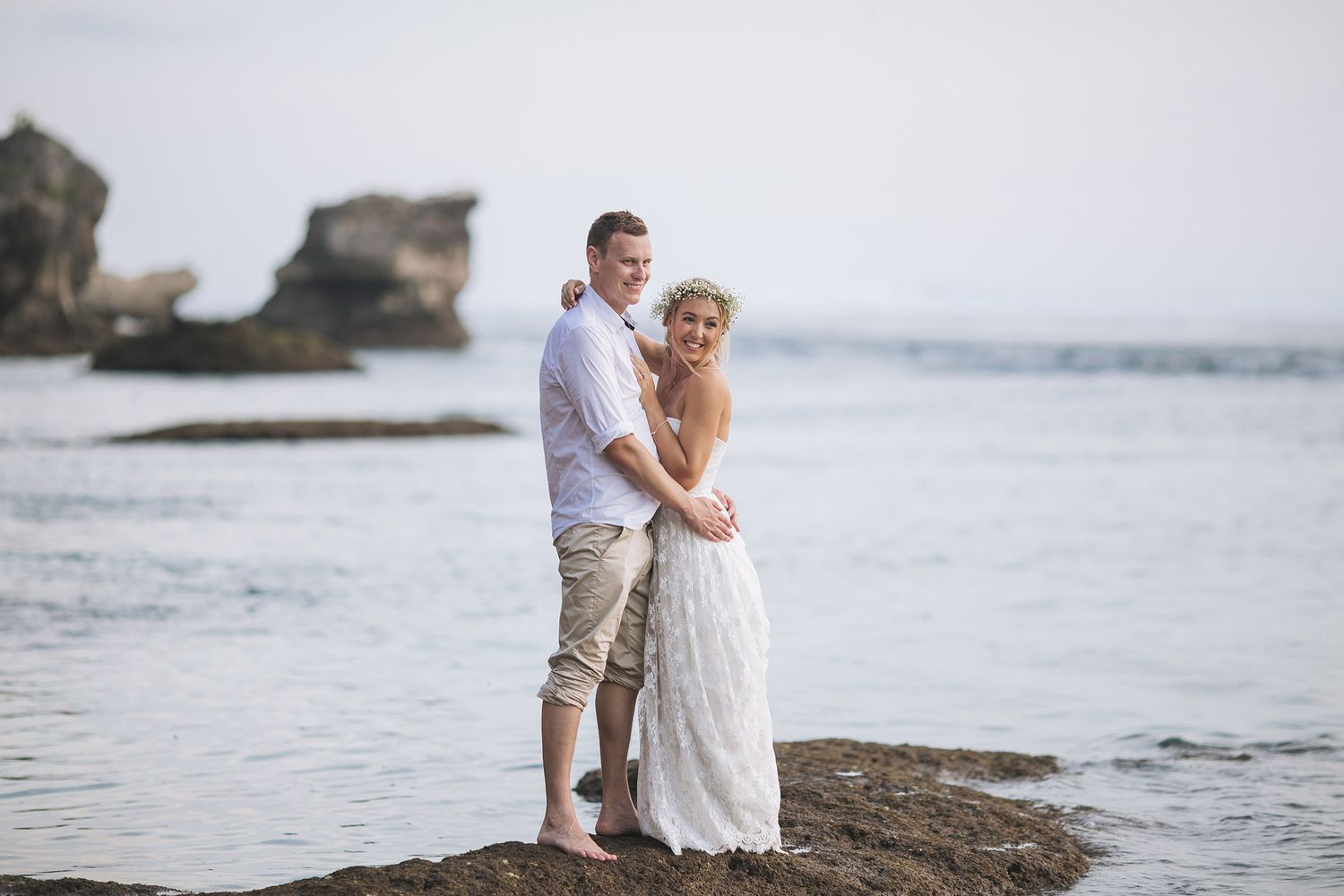 Newlyweds pose together on rocky coastal cliffs by the ocean.