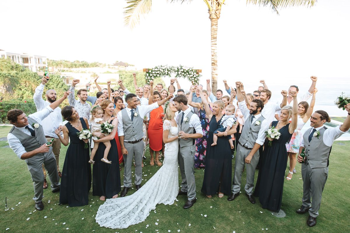 Wedding guests celebrating and cheering on a grassy lawn during an outdoor celebration.
