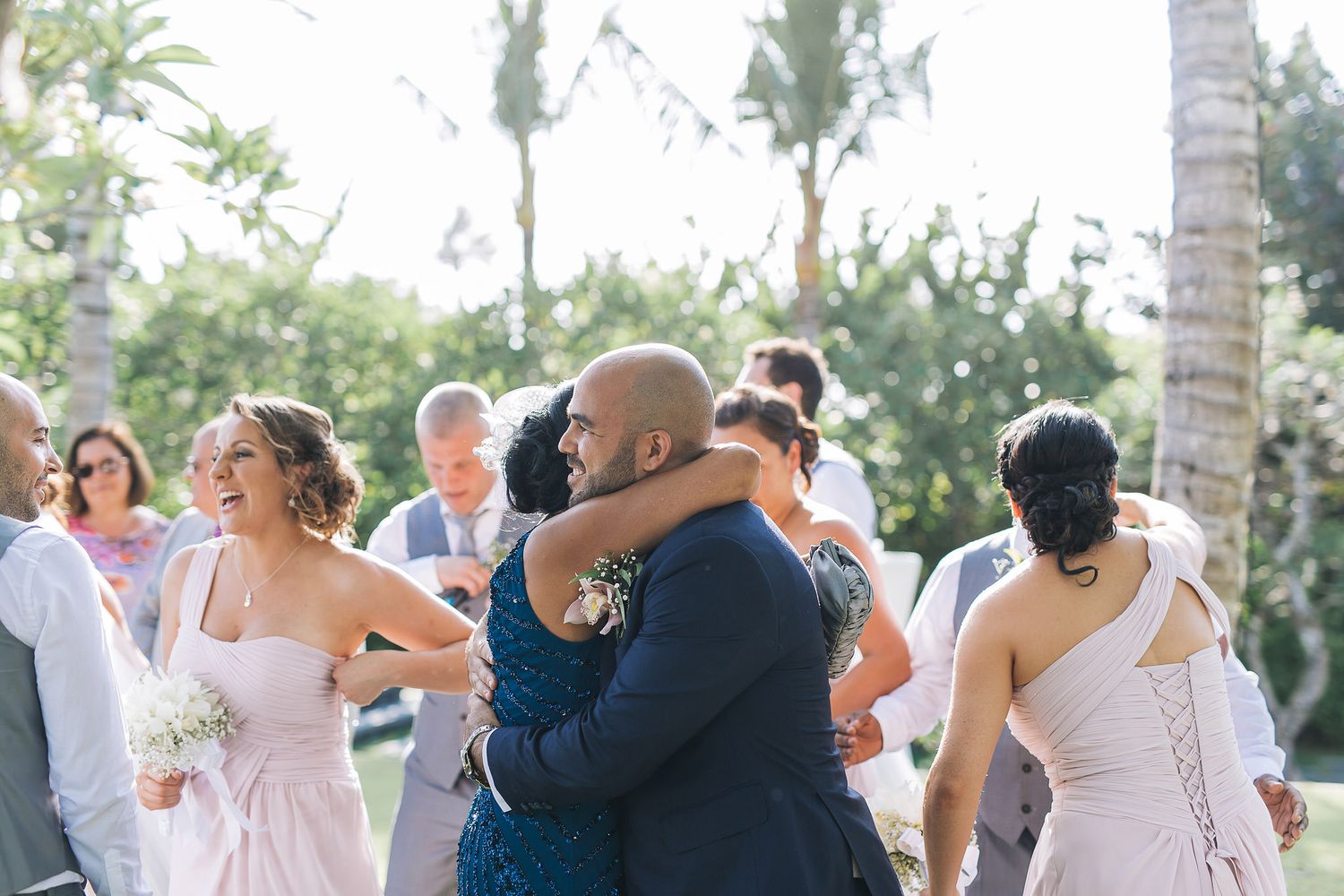 Wedding guests dancing and celebrating at outdoor tropical reception with palm trees in background.