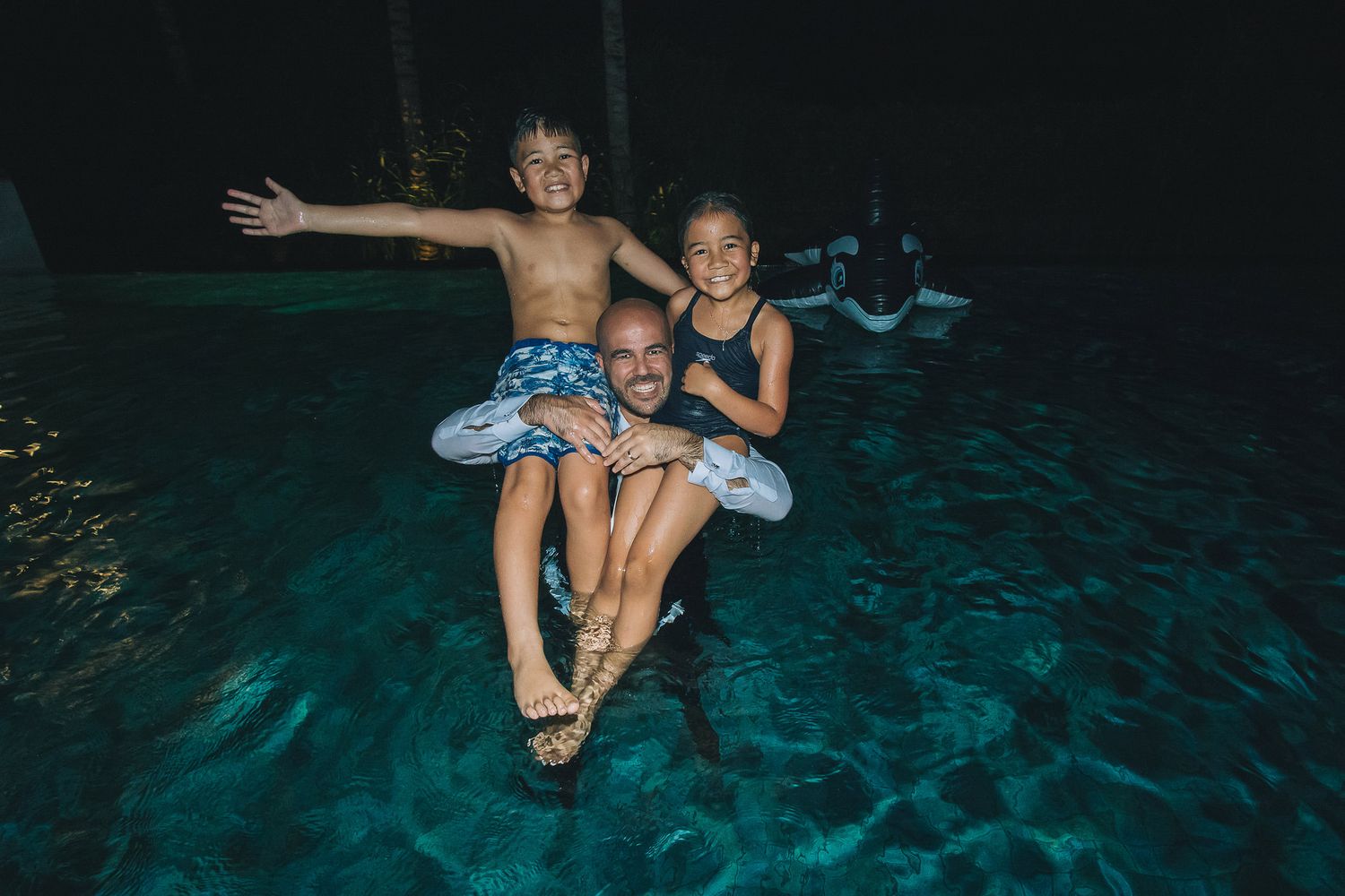 Two children playing and posing in a glowing blue cenote pool at night.