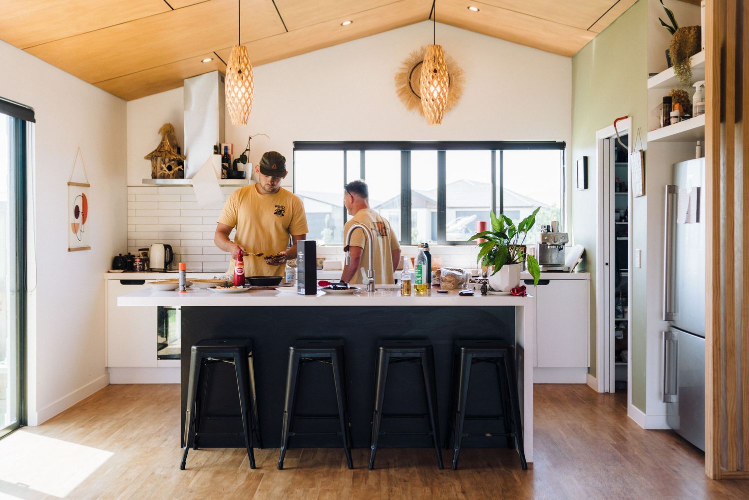 Modern kitchen with wooden ceiling, pendant light and black island counter in open concept space.