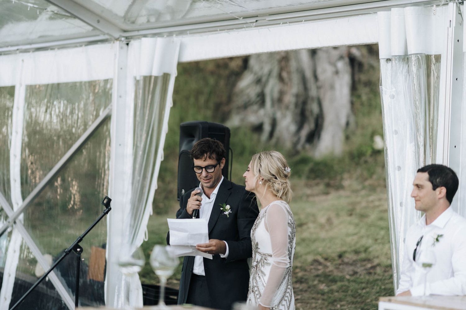 Wedding ceremony takes place under an elegant white gazebo in a natural outdoor setting.