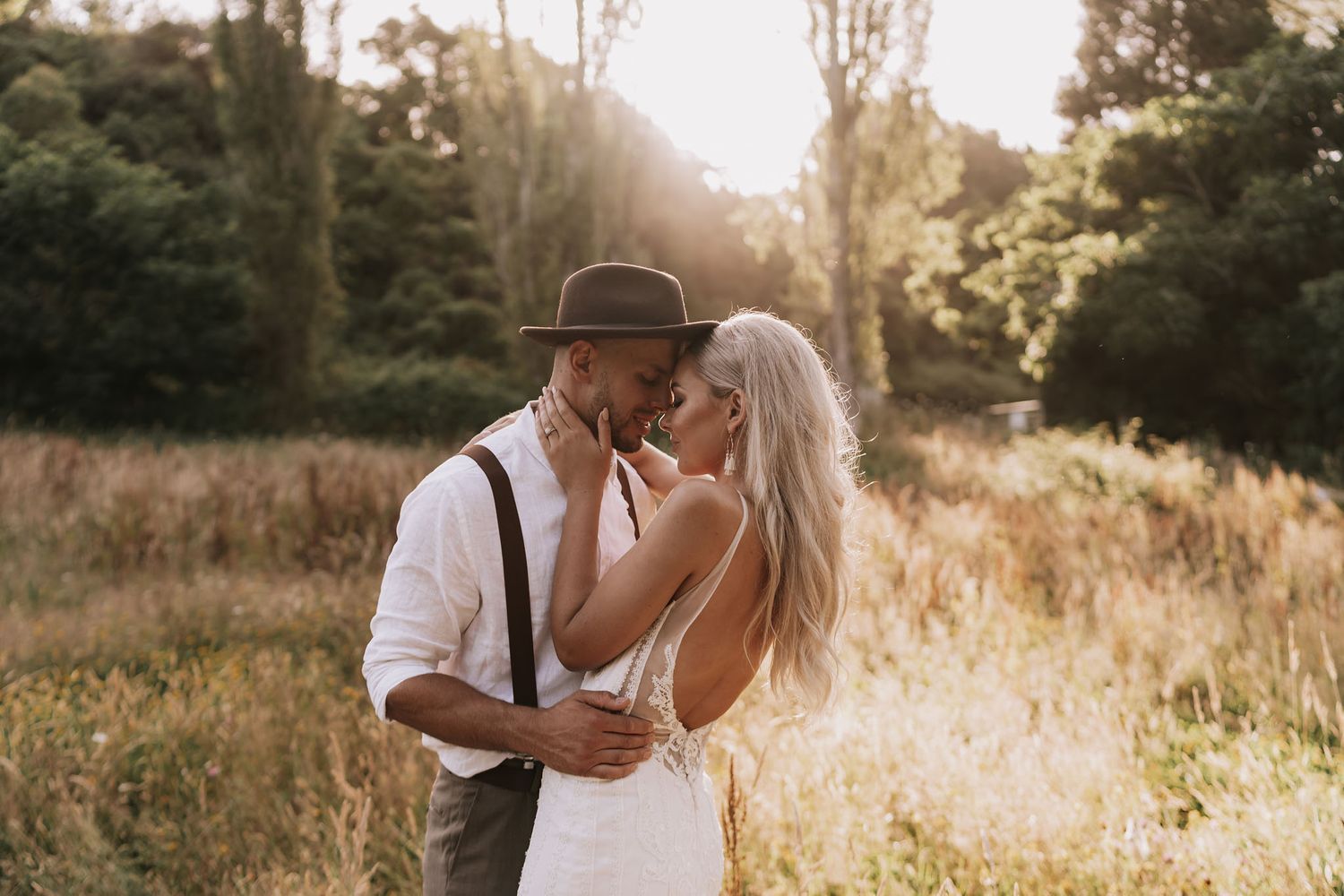 A couple shares an intimate moment in suspenders and lace while standing in a golden meadow at sunset.