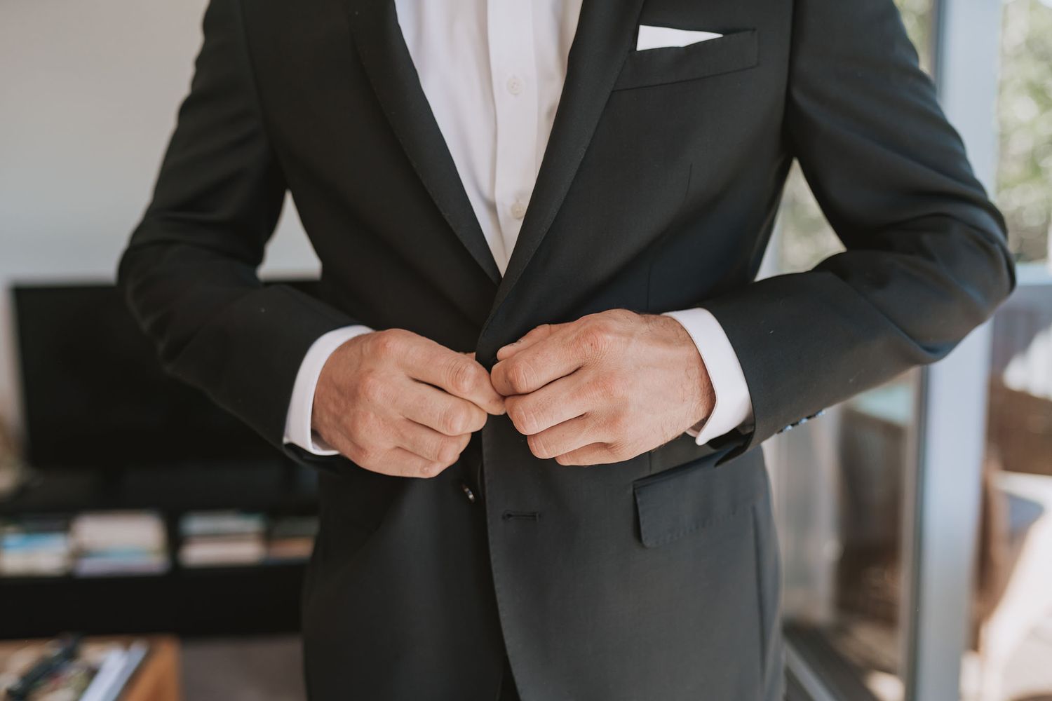 Close-up view of someone buttoning a classic black tuxedo jacket with white dress shirt underneath.