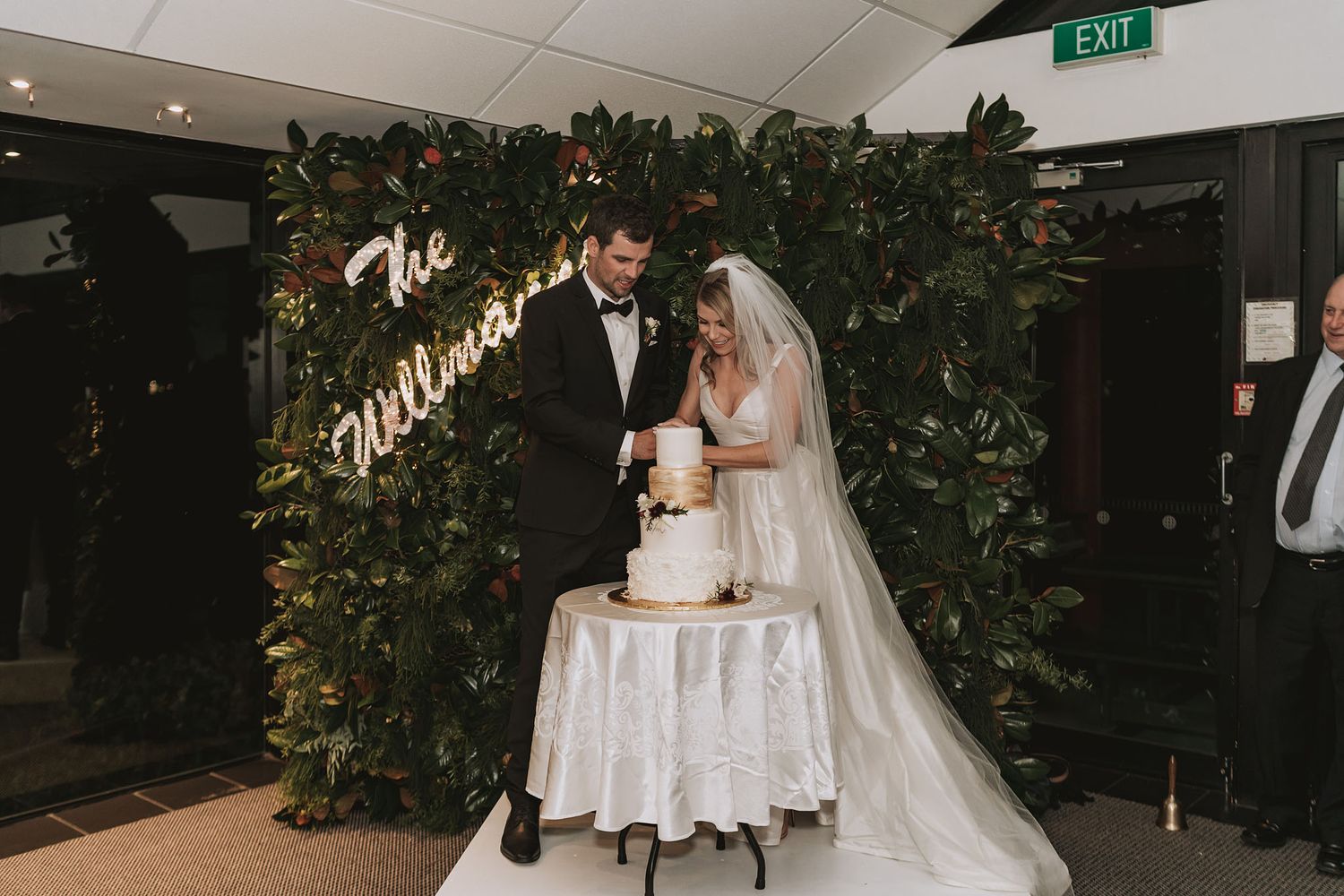A wedding reception space adorned with greenery, white decor, and soft lighting creates an elegant atmosphere.