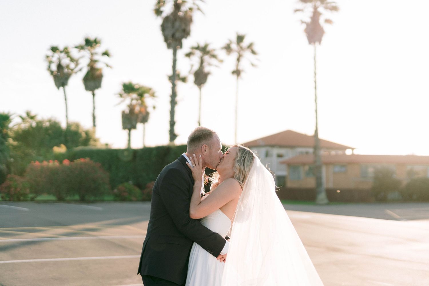 Romantic sunset wedding portrait with palm trees silhouetted in the background.