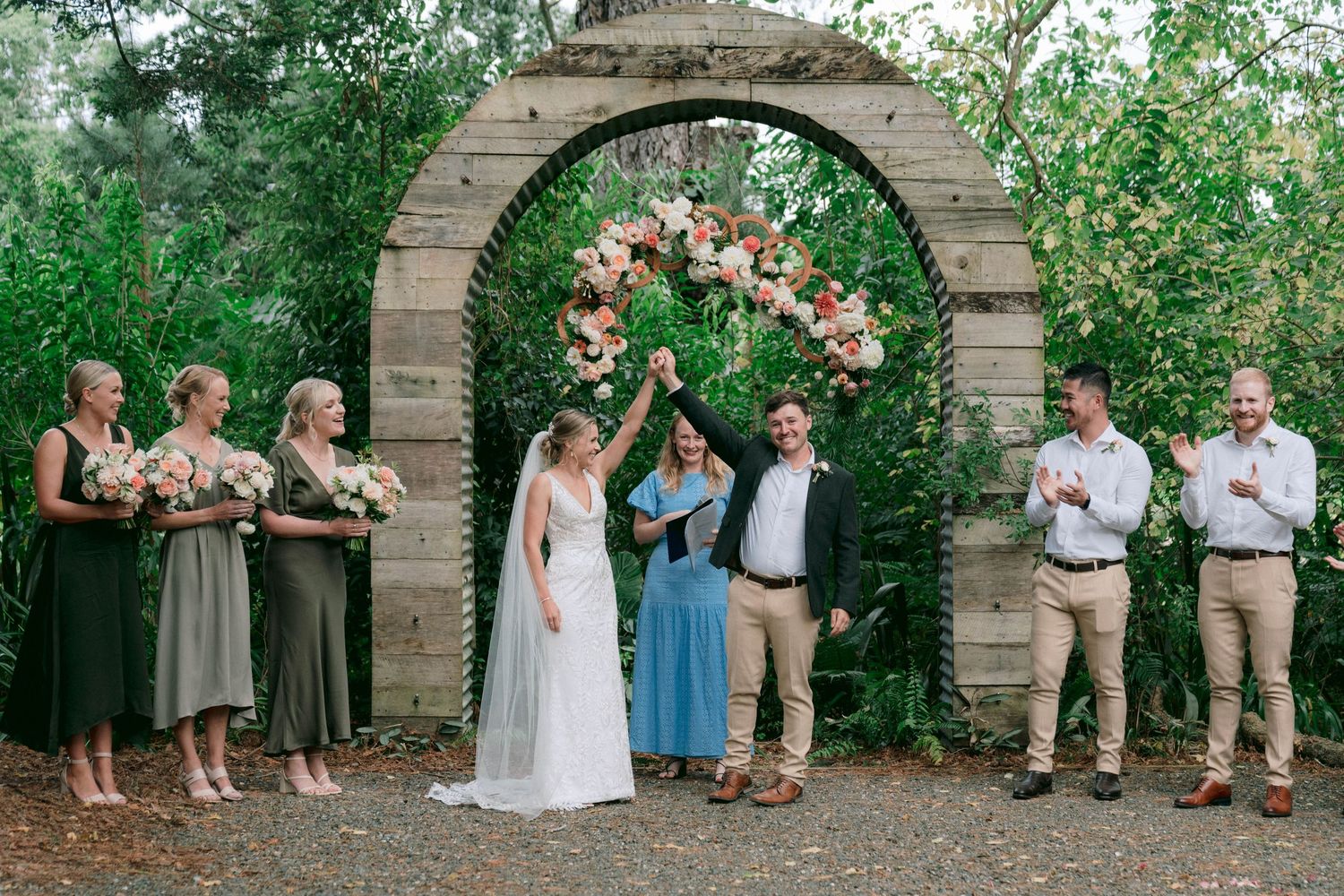 Wedding party posing under stone archways in a garden setting.