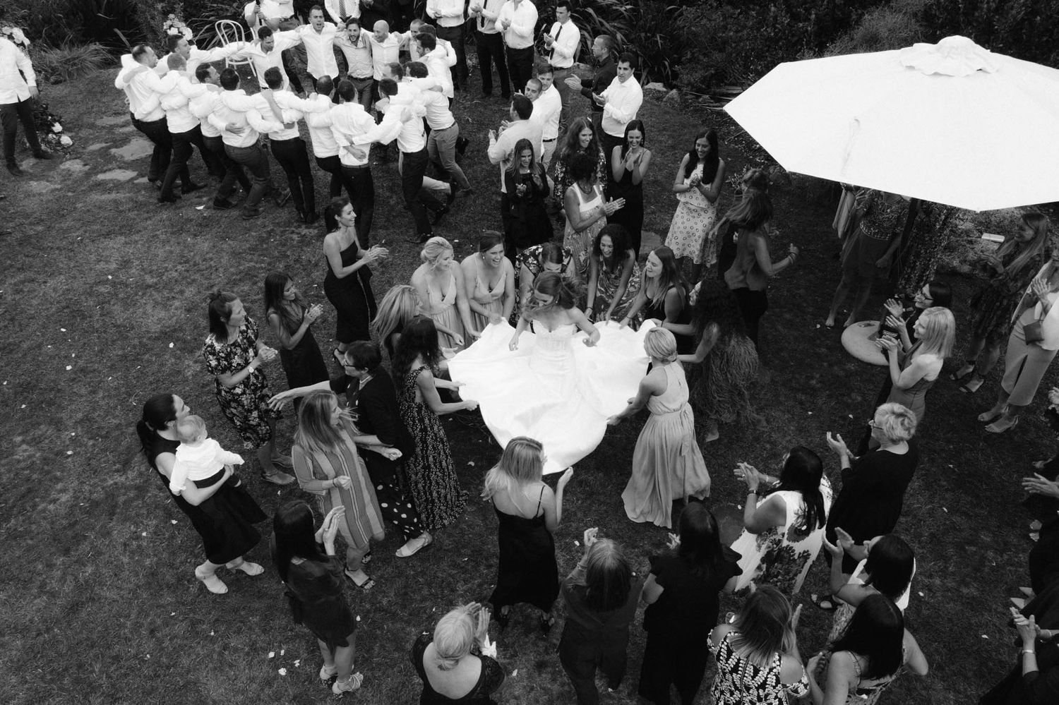 Aerial black and white view of people gathered around tables under a canopy at an outdoor social event.