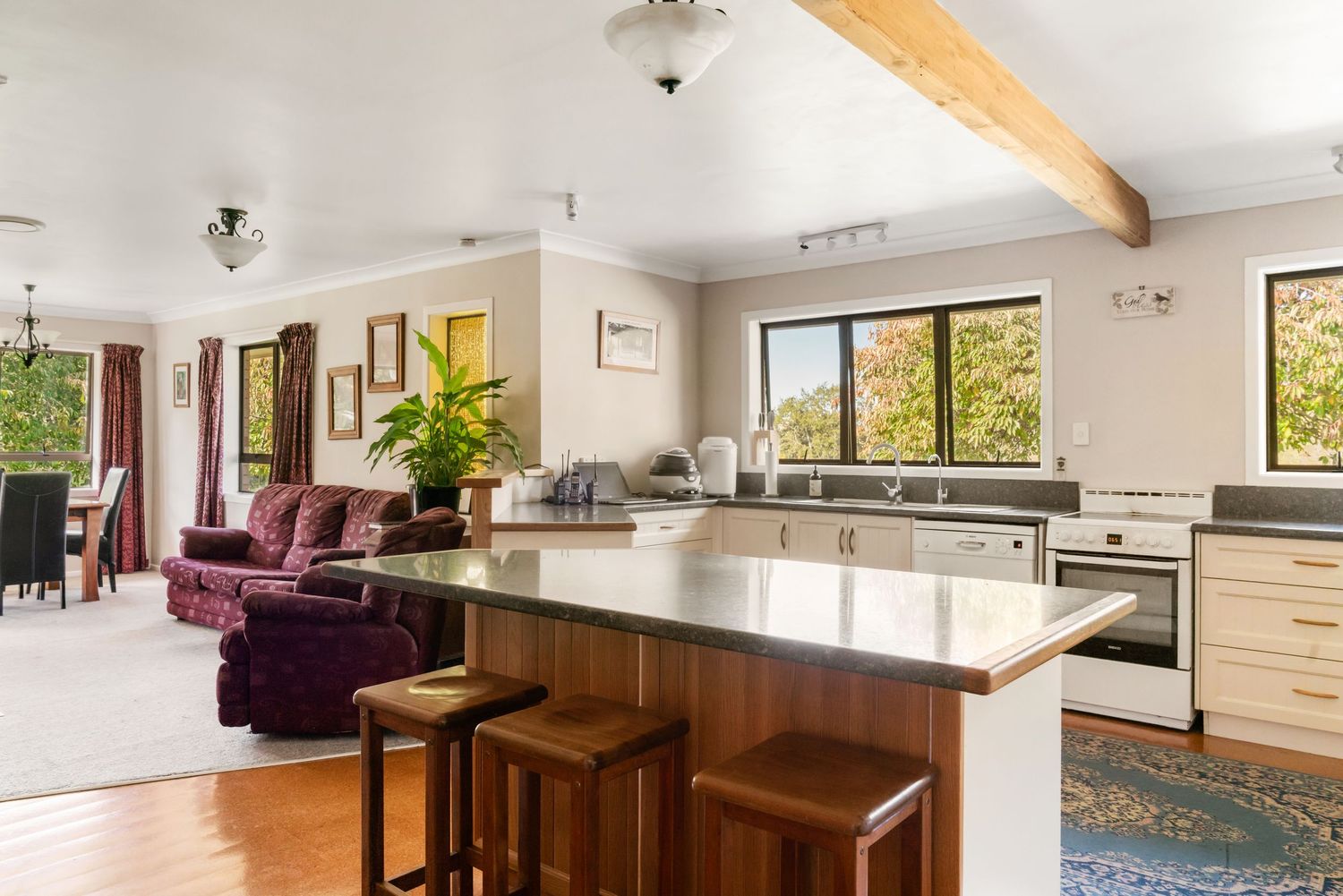 Modern open concept kitchen and living room with burgundy furniture and large windows.