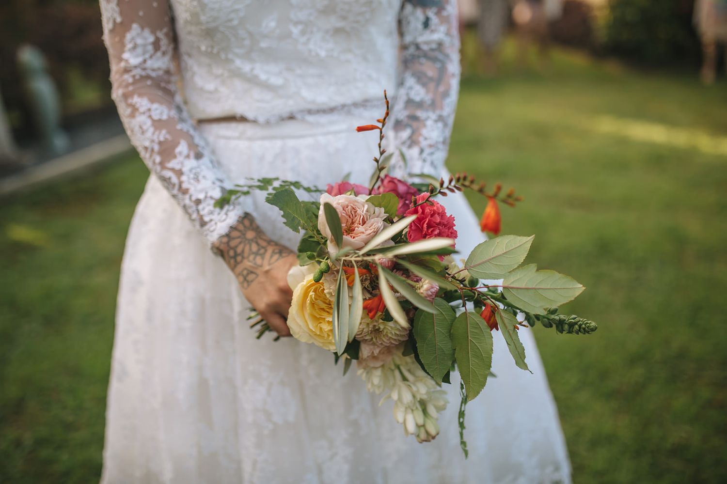 An elegant lace bridal dress detail with delicate floral bouquet against a green garden background.