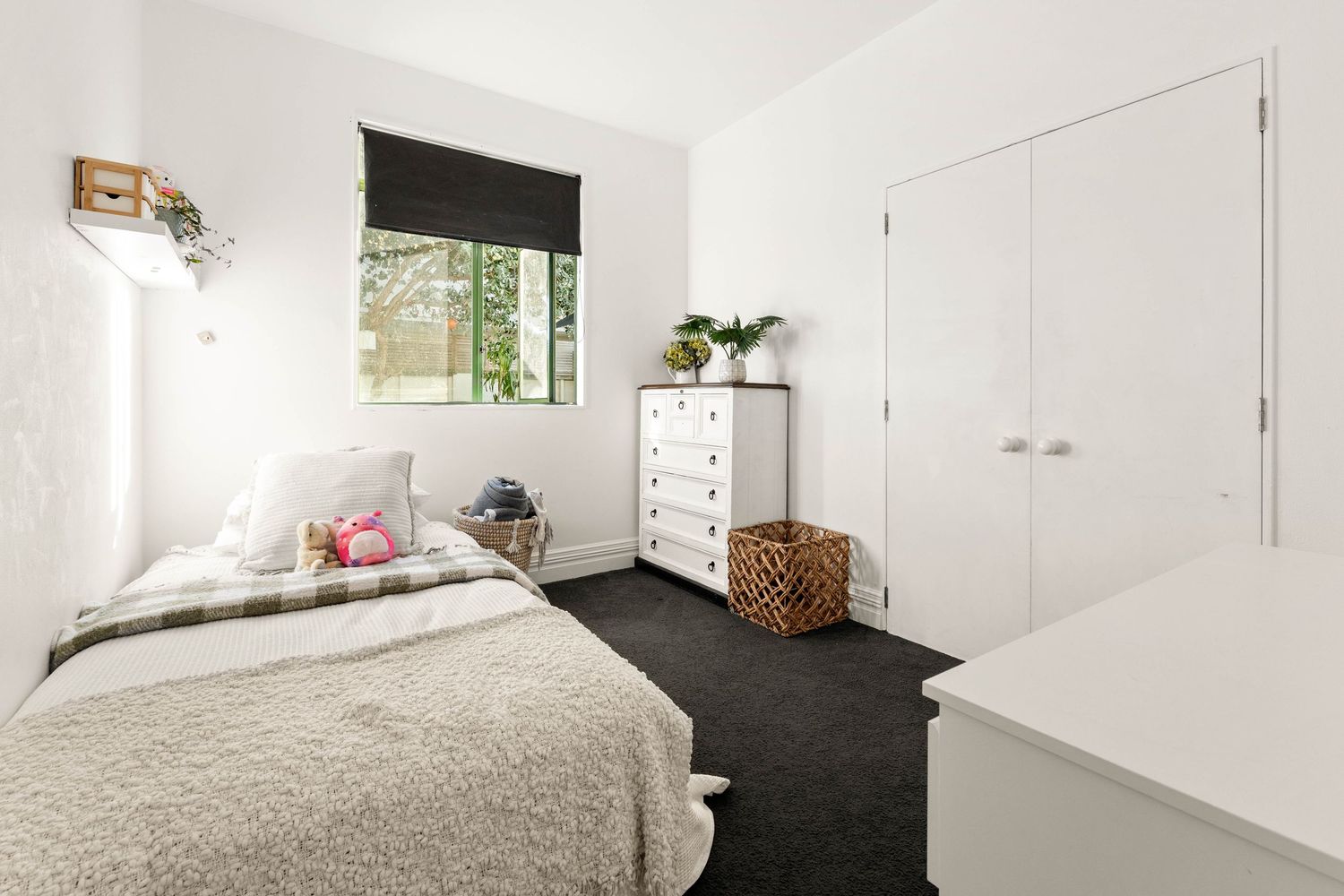 Minimalist bedroom with white walls, dark carpet, and built-in closet storage.
