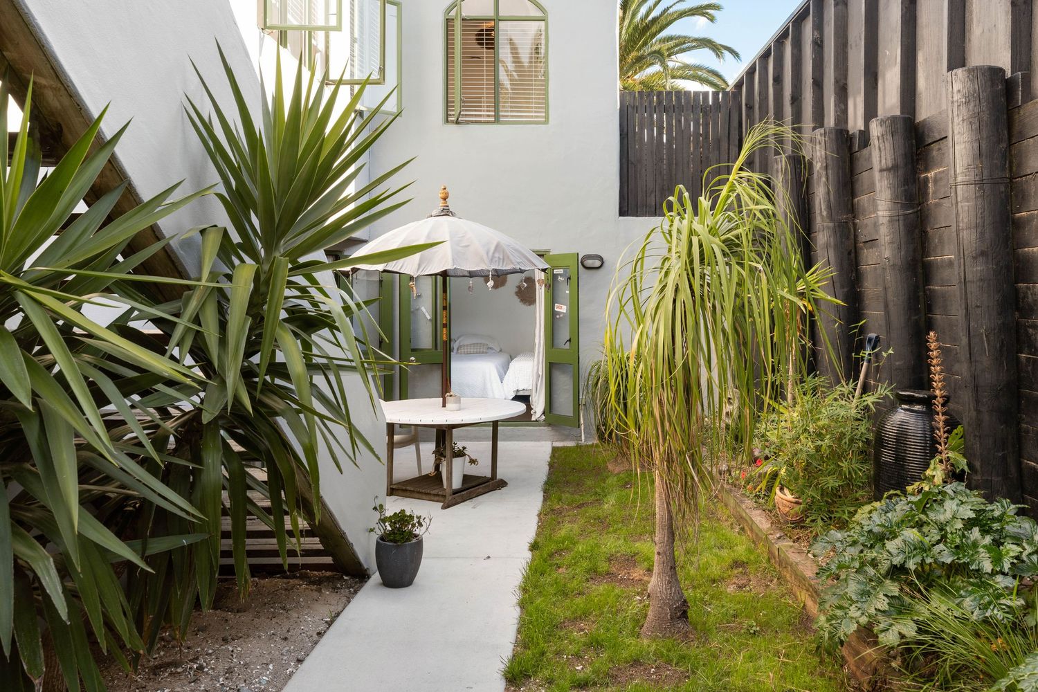 Narrow side yard with tropical plants, bamboo privacy fence, and white exterior walls.