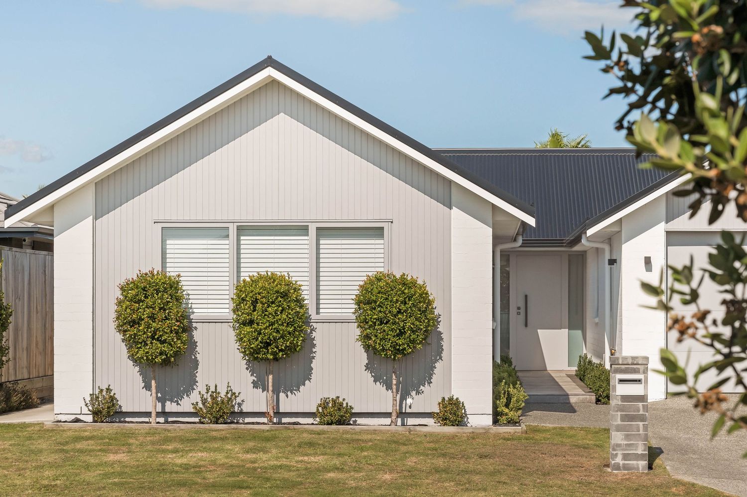 Modern white farmhouse exterior with clean lines and three evenly spaced trees in front landscape design.