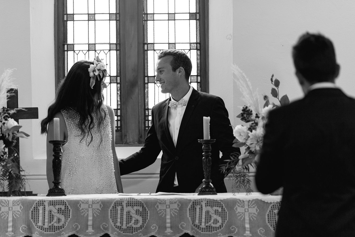 Black and white photograph of a wedding ceremony taking place at an altar with stained glass windows in the background.