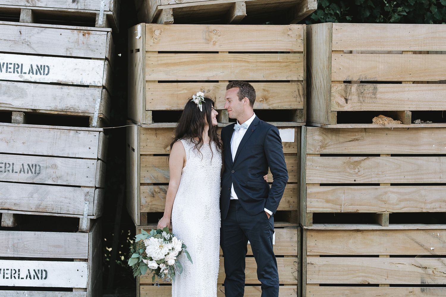 Newlywed couple poses romantically against rustic wooden crates in an outdoor wedding setting.